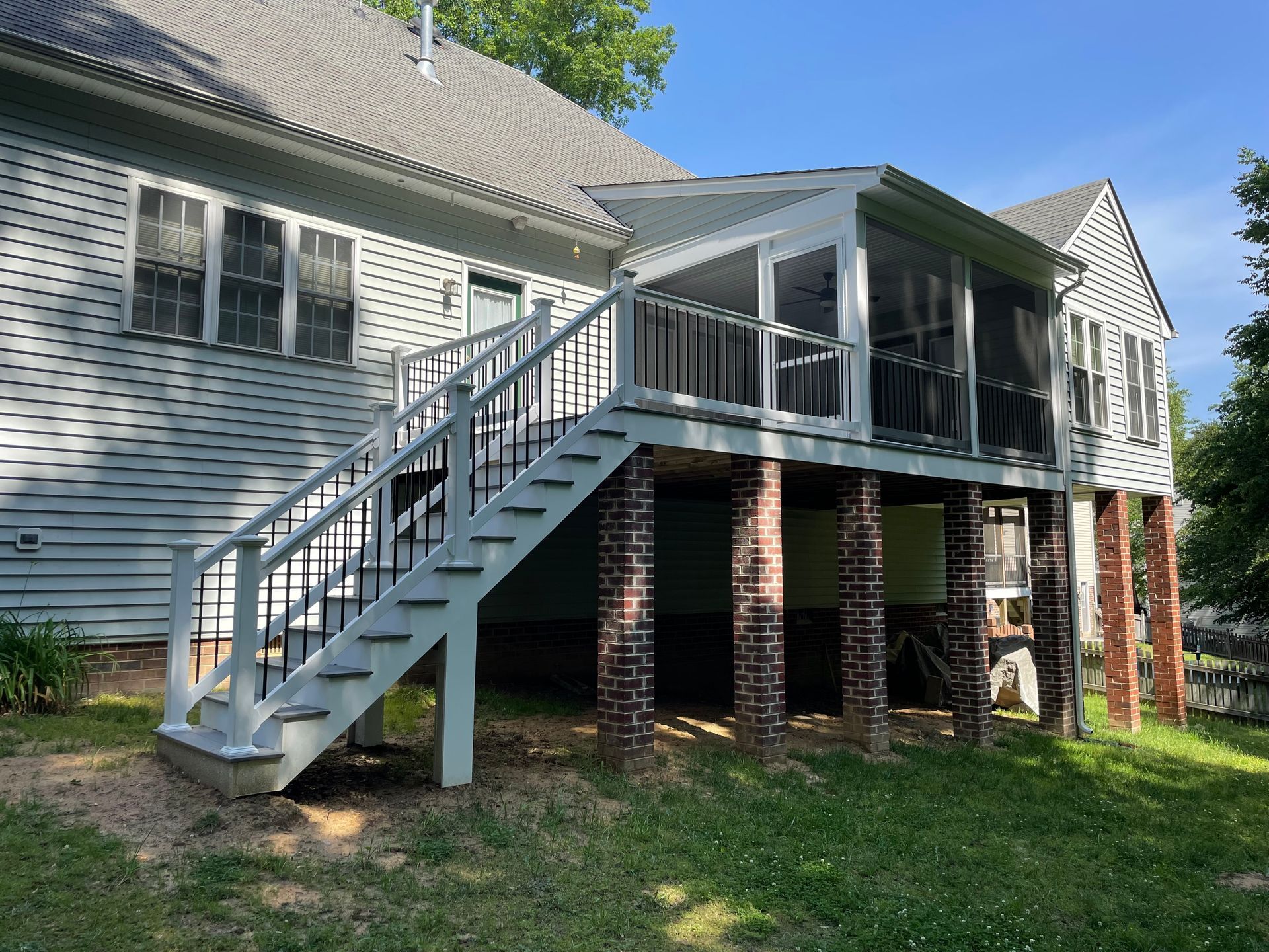 Raised deck with gray stairs and brick columns attached to a white house in a grassy yard