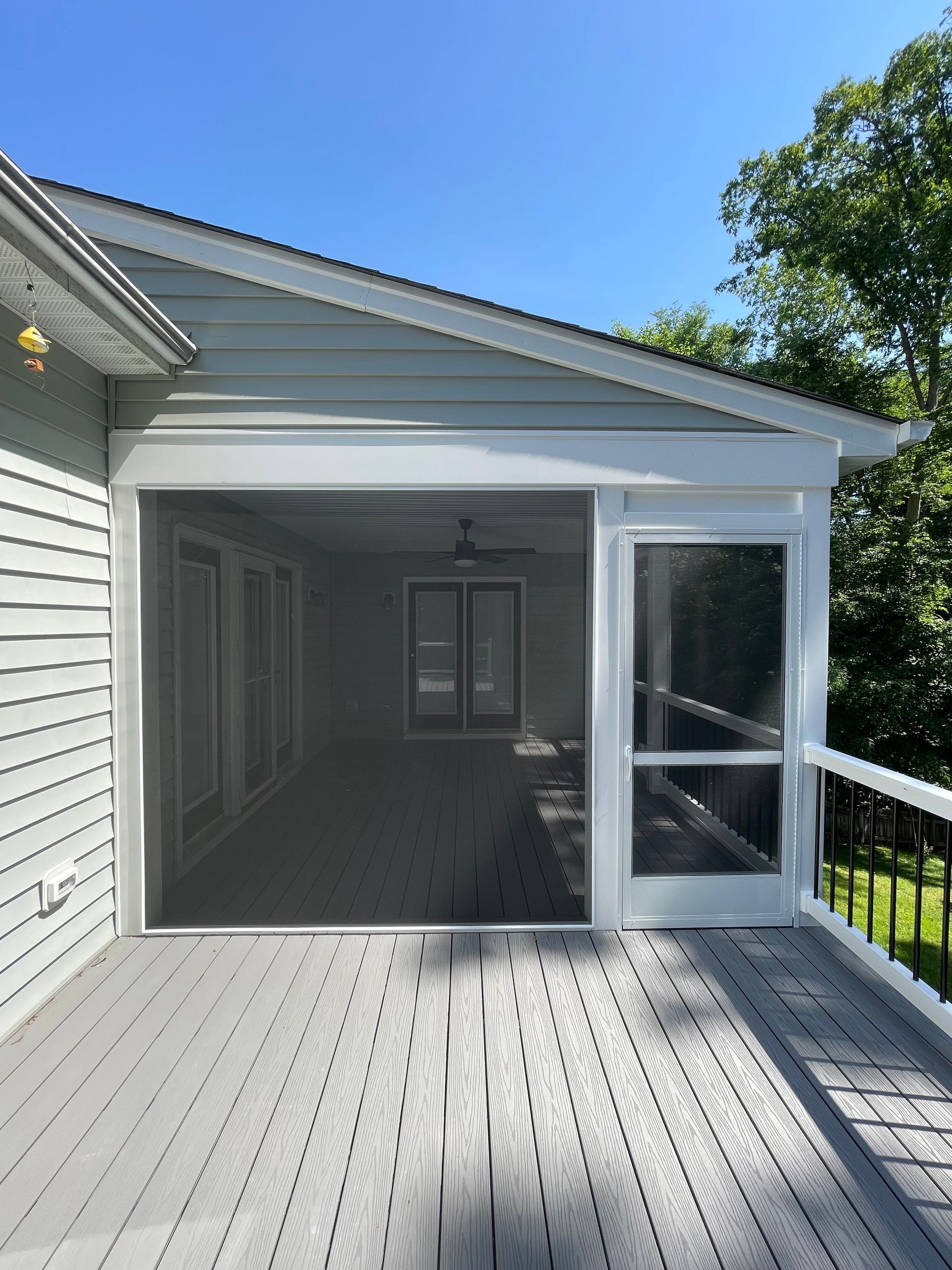 Covered wooden deck with an open screened porch and white siding under a blue sky