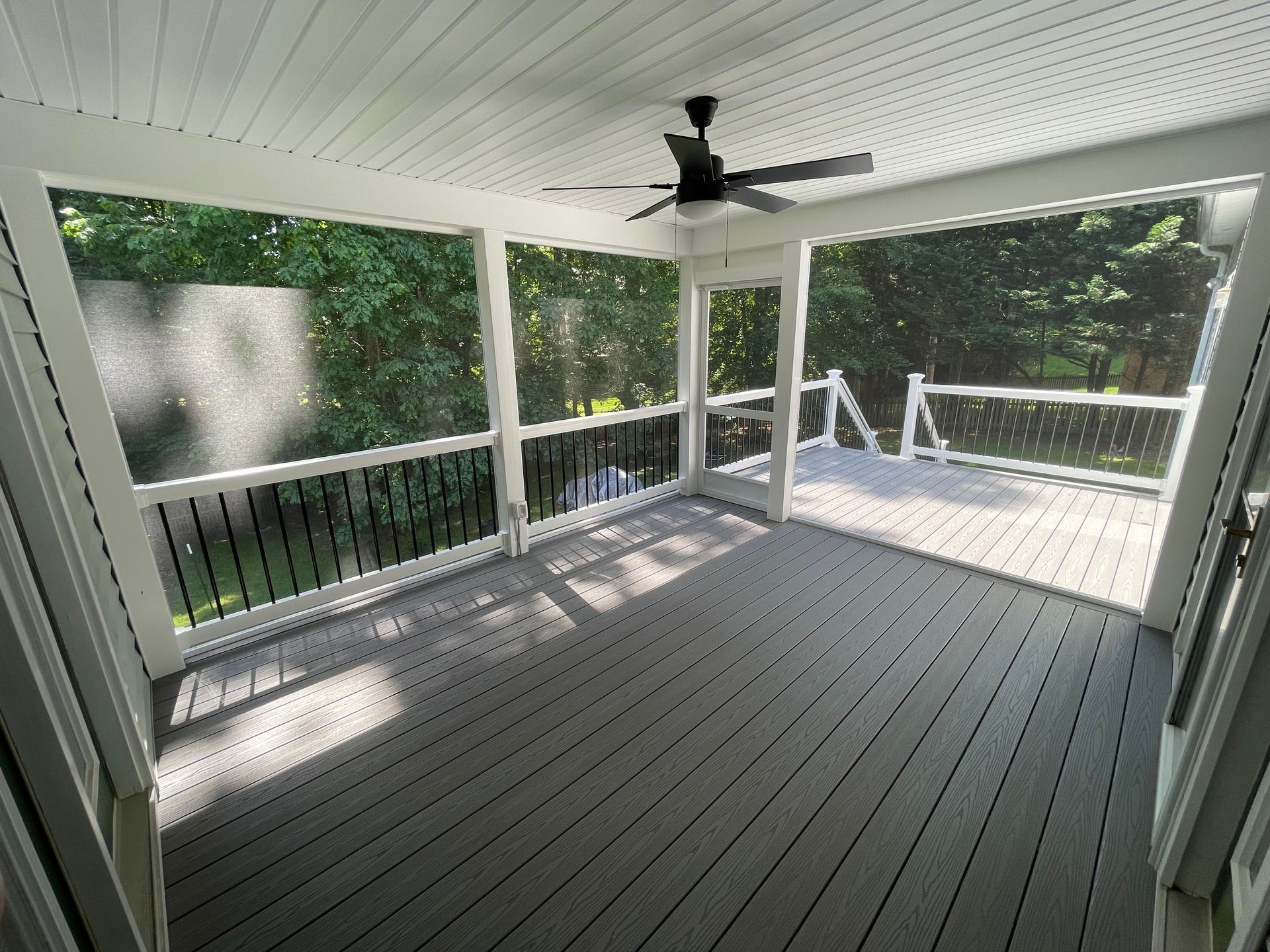 Covered porch with gray floor, white railings, and ceiling fan overlooking trees