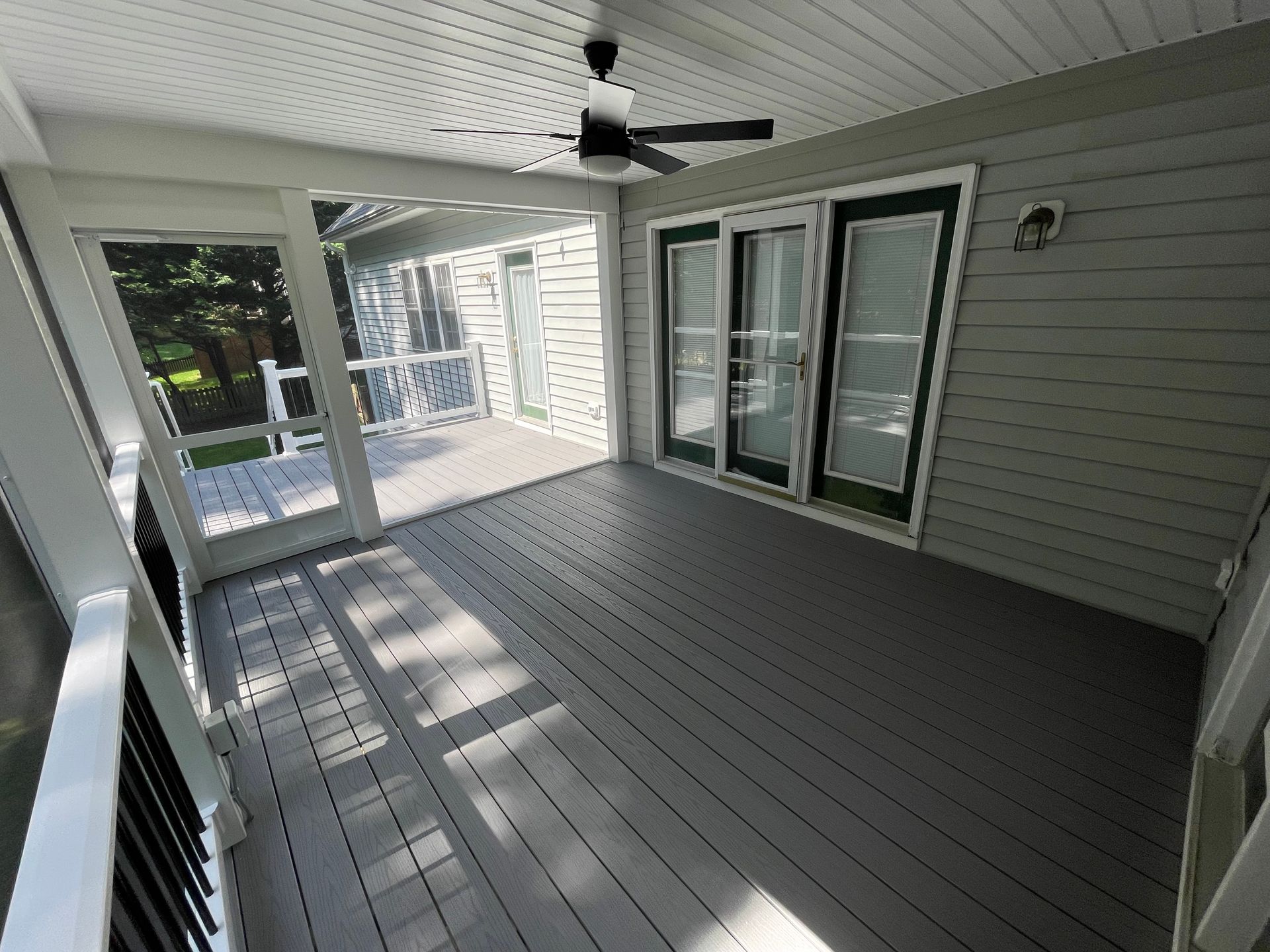 Covered porch with gray flooring, white siding, ceiling fan, and sliding glass doors.