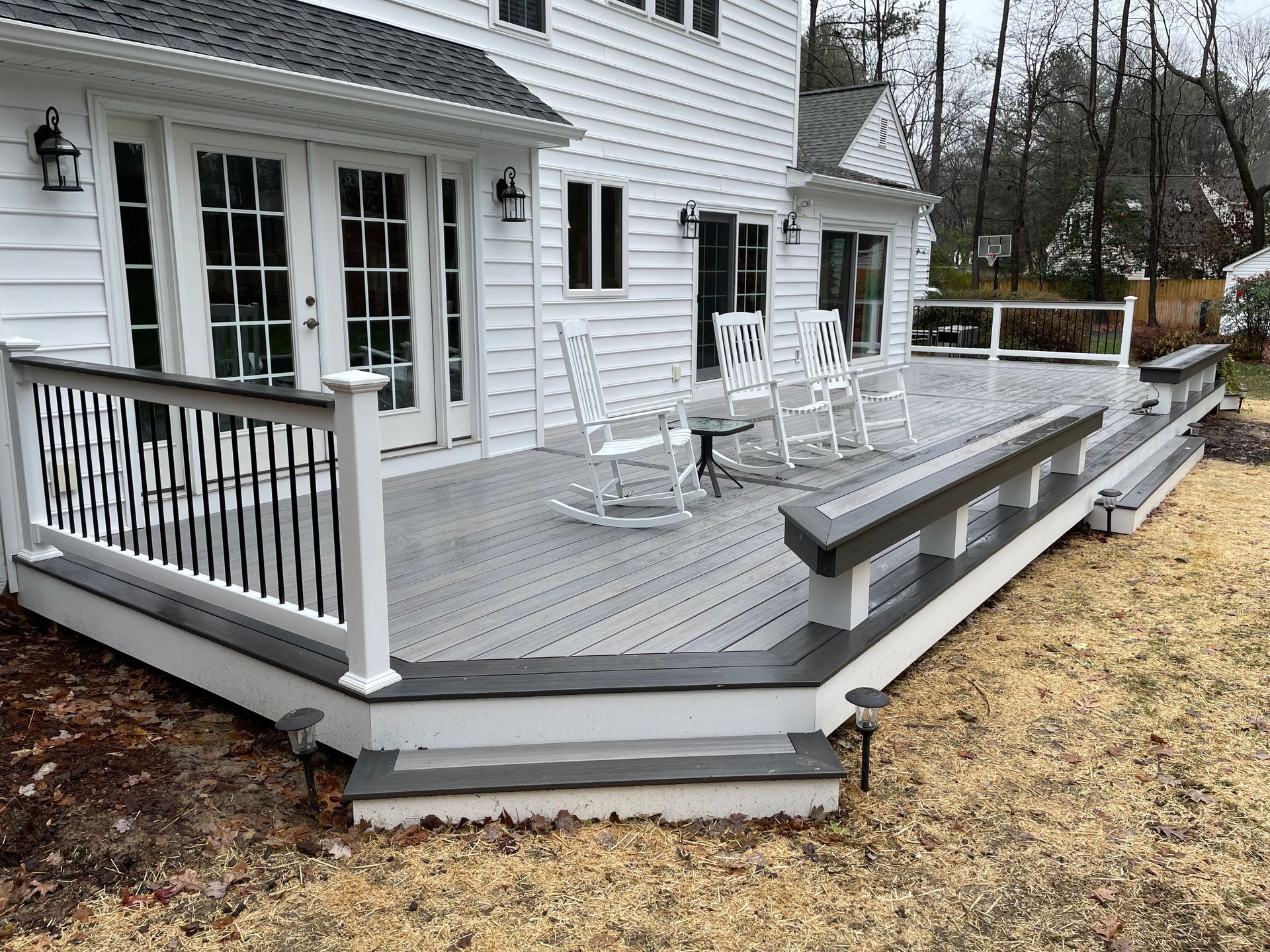 White house deck with gray railing and rocking chairs beside a yard.