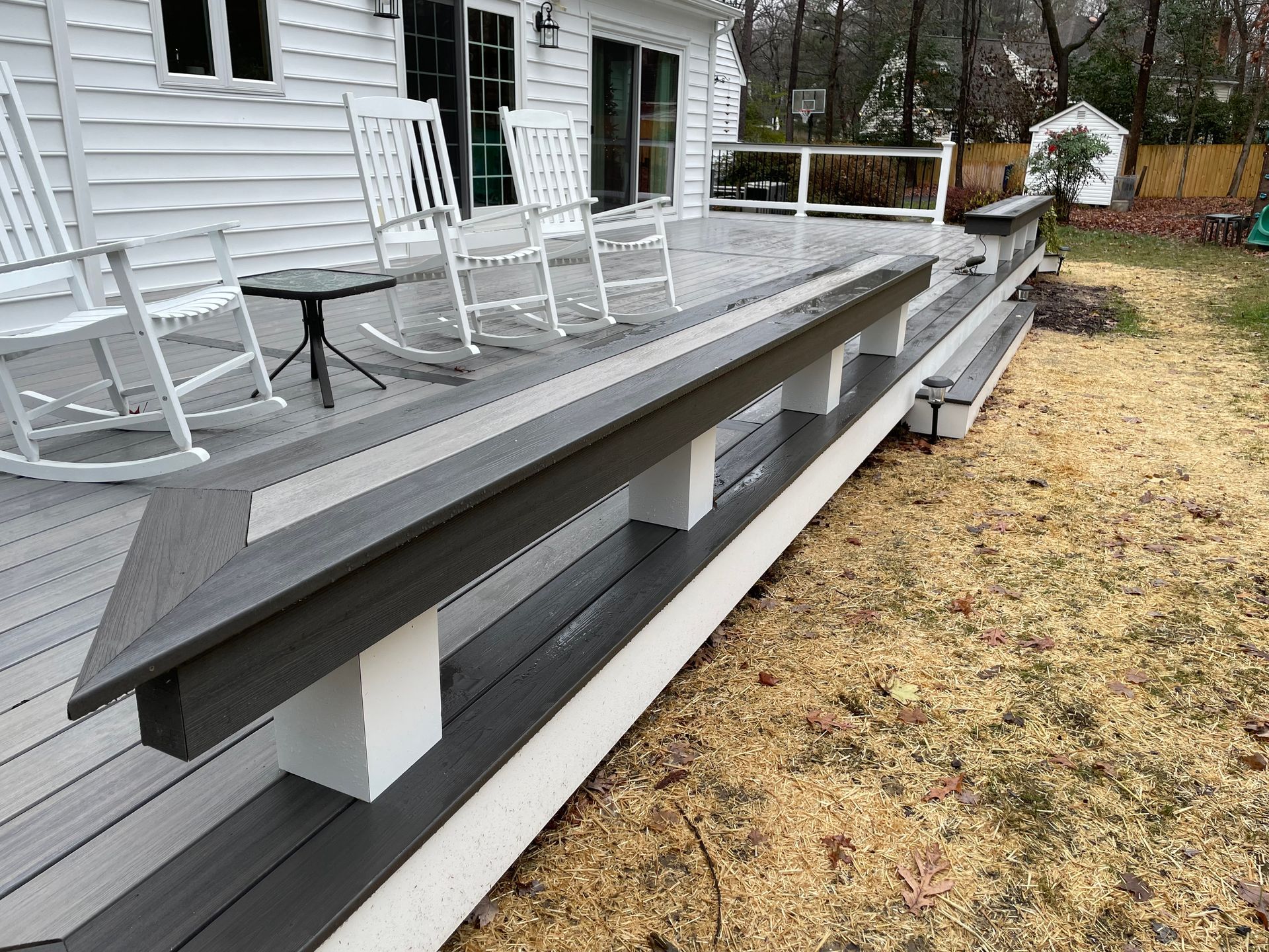 Long gray ramp beside a white house porch with rocking chairs and a small table