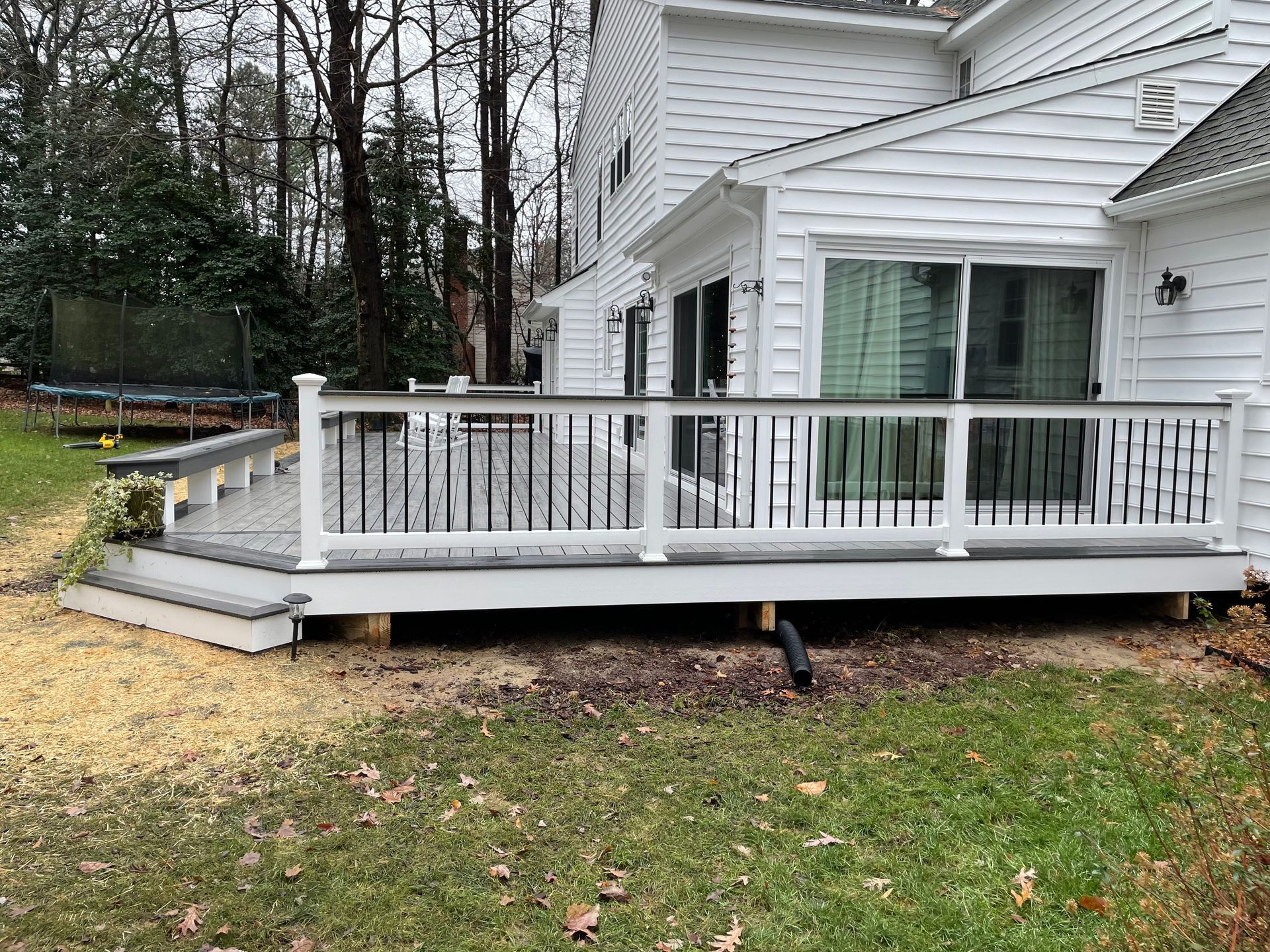 White house back deck with railing and steps in a wooded yard