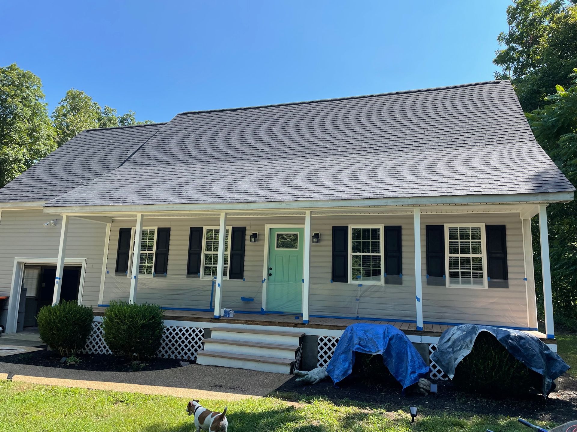 Single-story beige house with dark gray shingled roof, mint-green front door, and covered items on the porch.
