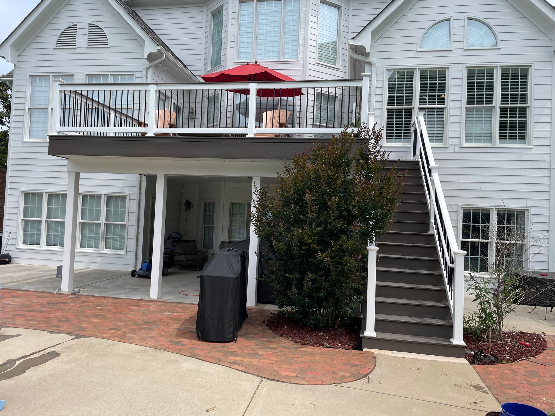 Raised deck with white railings, red patio umbrella, and stairs leading down to a brick patio.