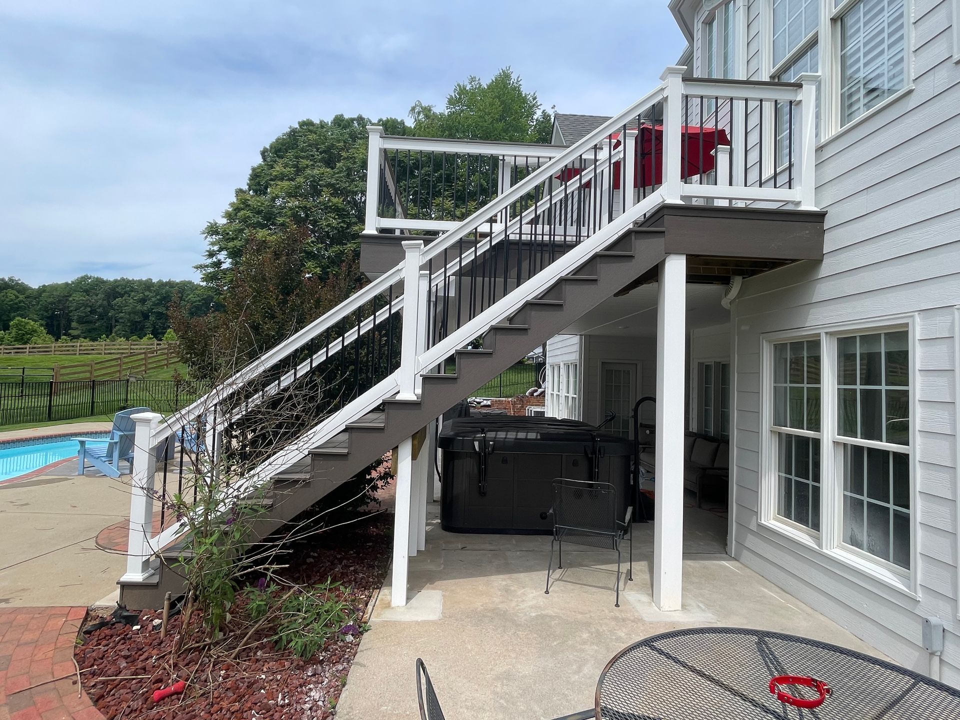 Backyard deck staircase with white railings beside a house and swimming pool