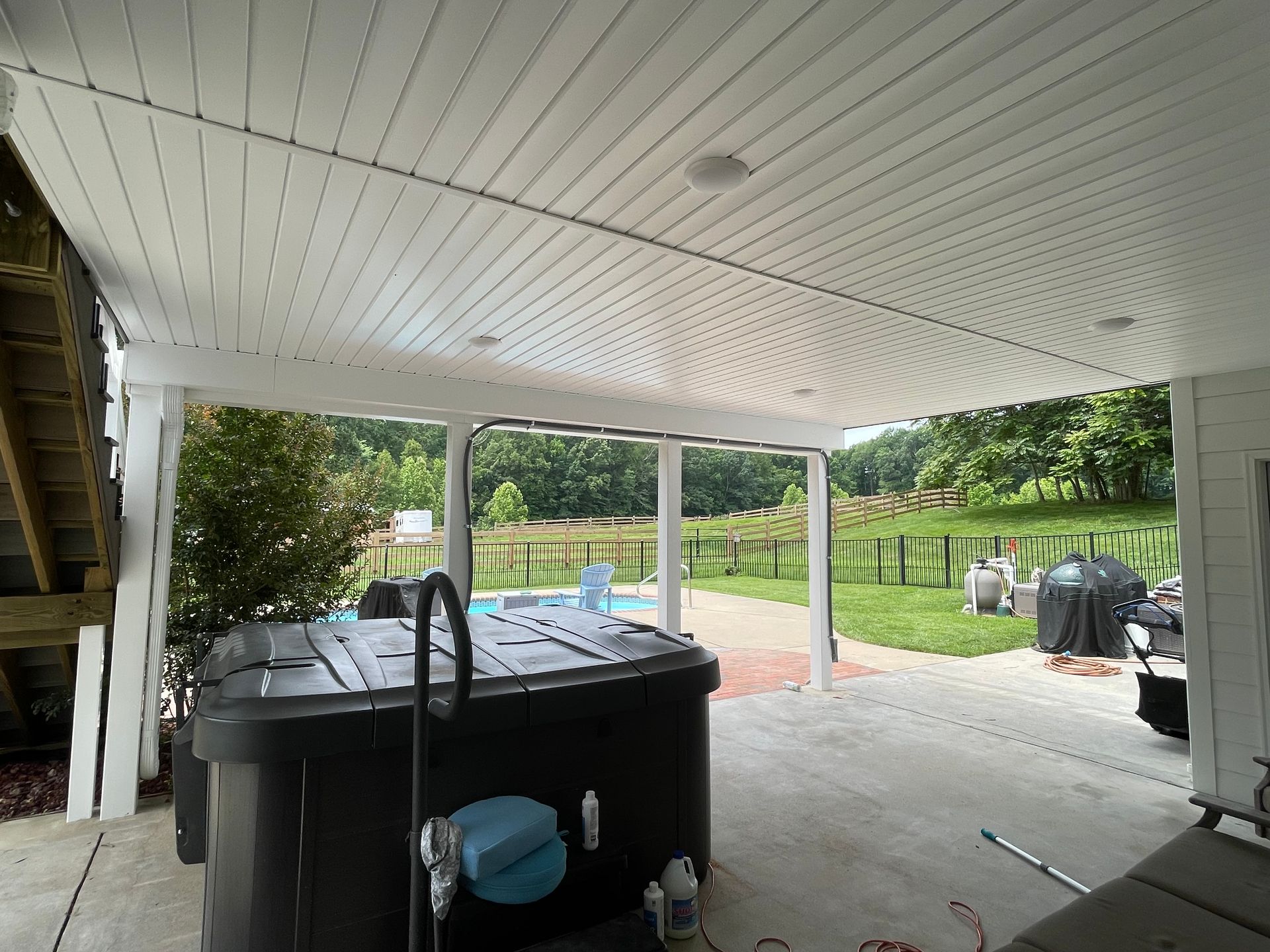 Covered patio with a hot tub, stairs on the left, and a backyard lawn beyond.