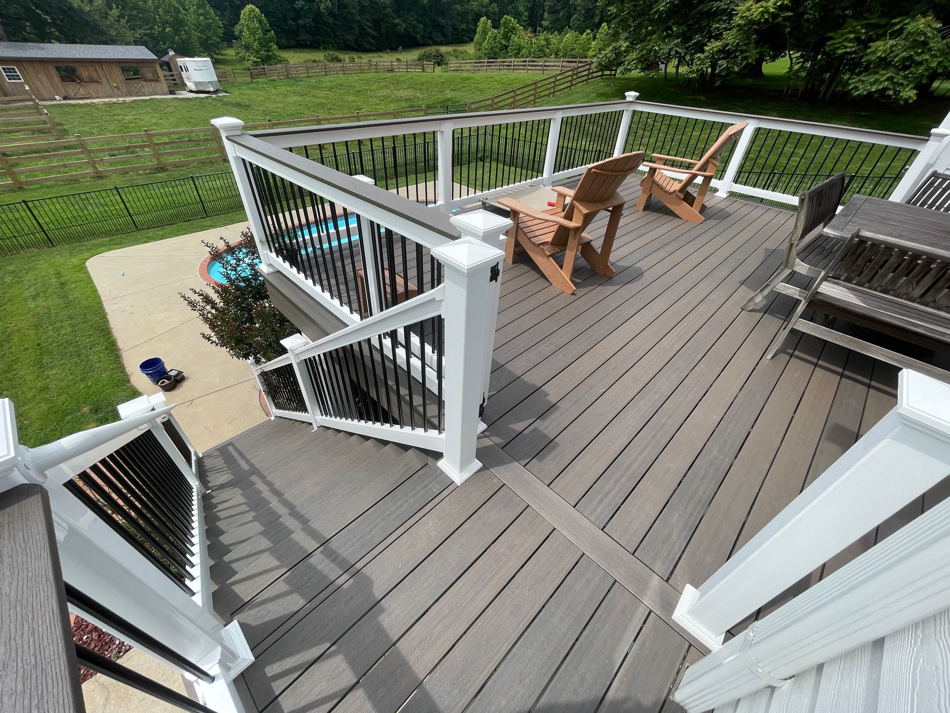 Wooden deck with patio chairs and table, white railing, and steps overlooking a yard and garden.