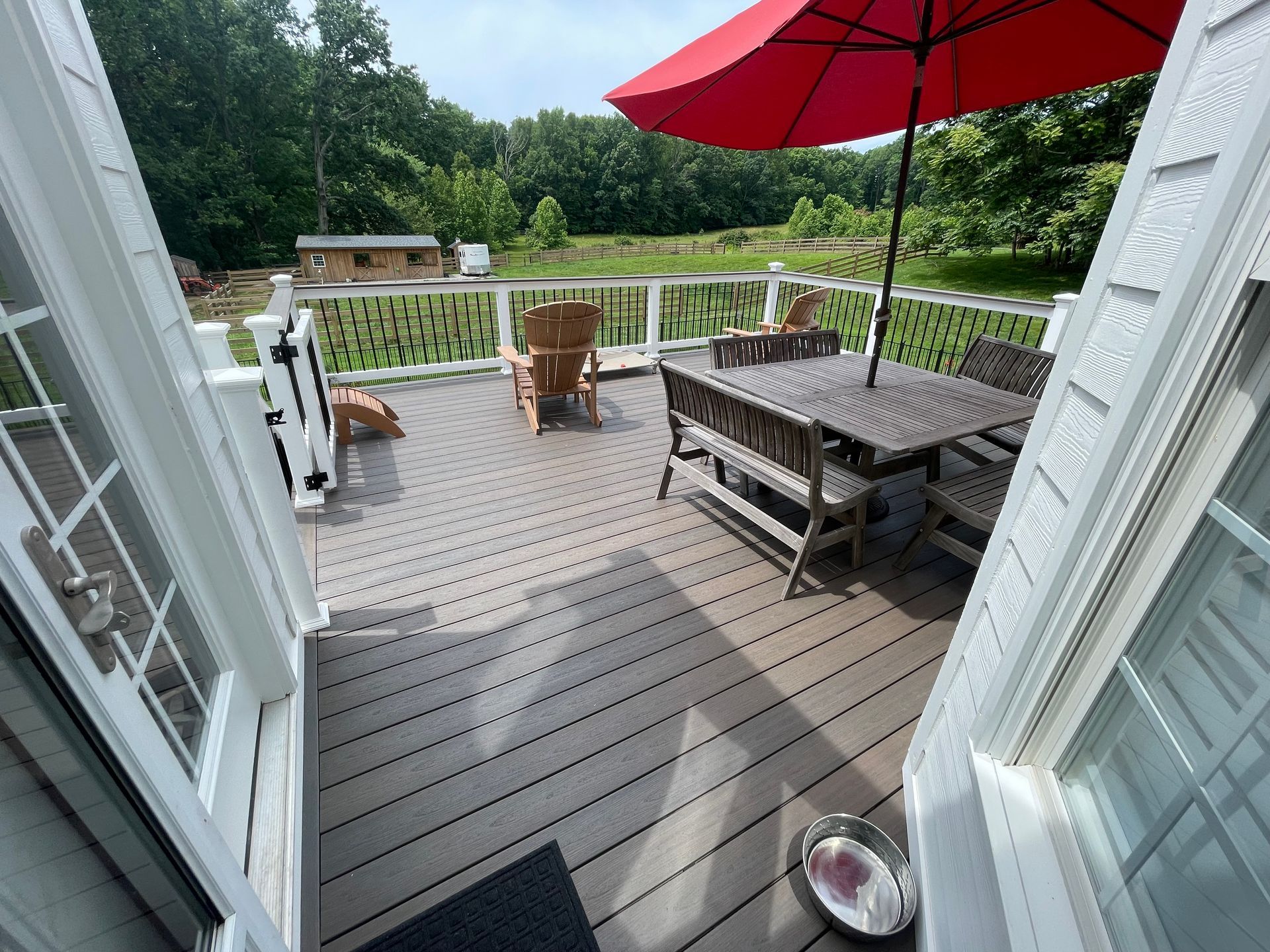 Deck with patio table, red umbrella, chairs, and a yard view through open French doors.