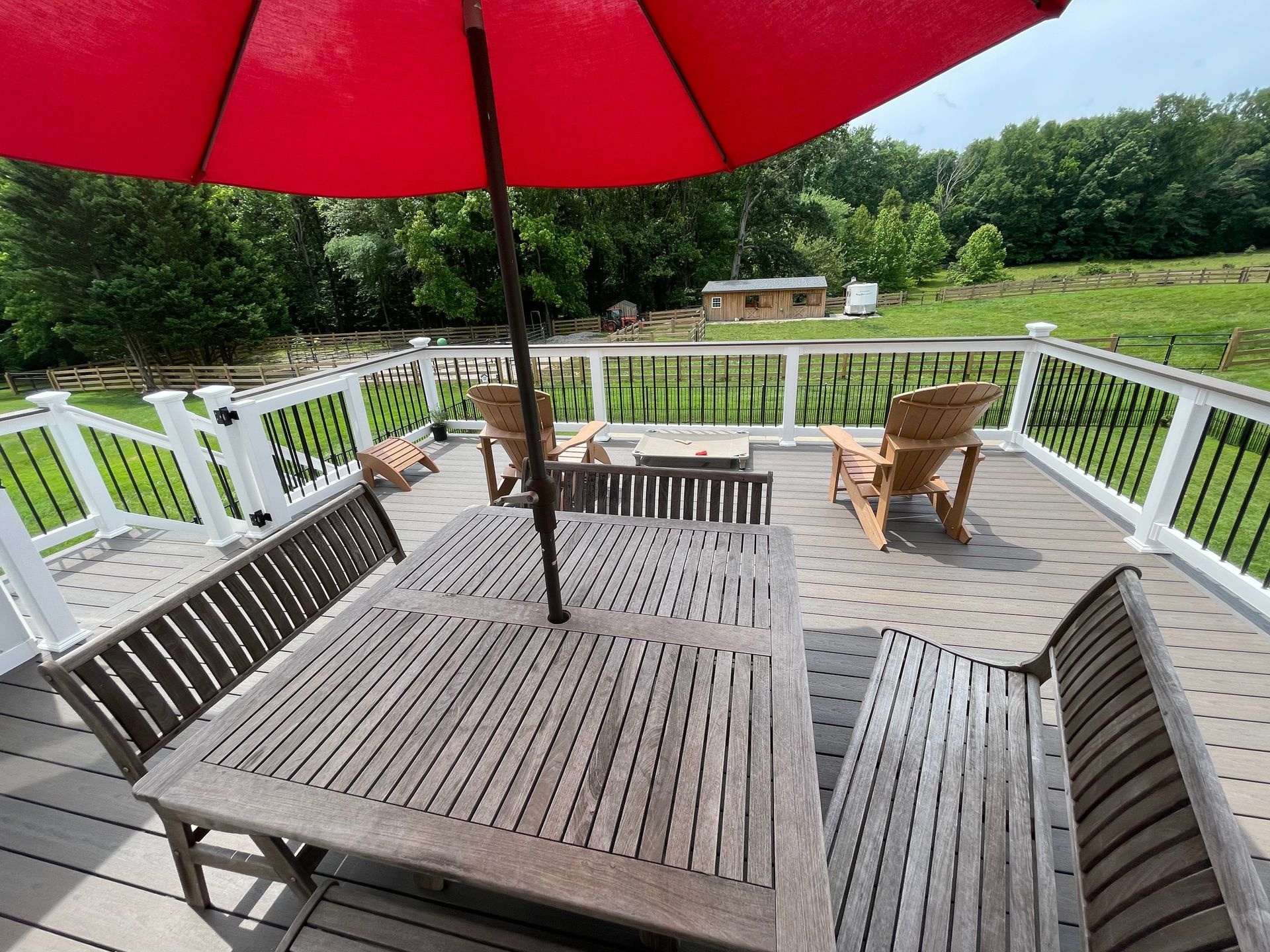Deck with red umbrella, wooden table and chairs, overlooking a green yard and trees