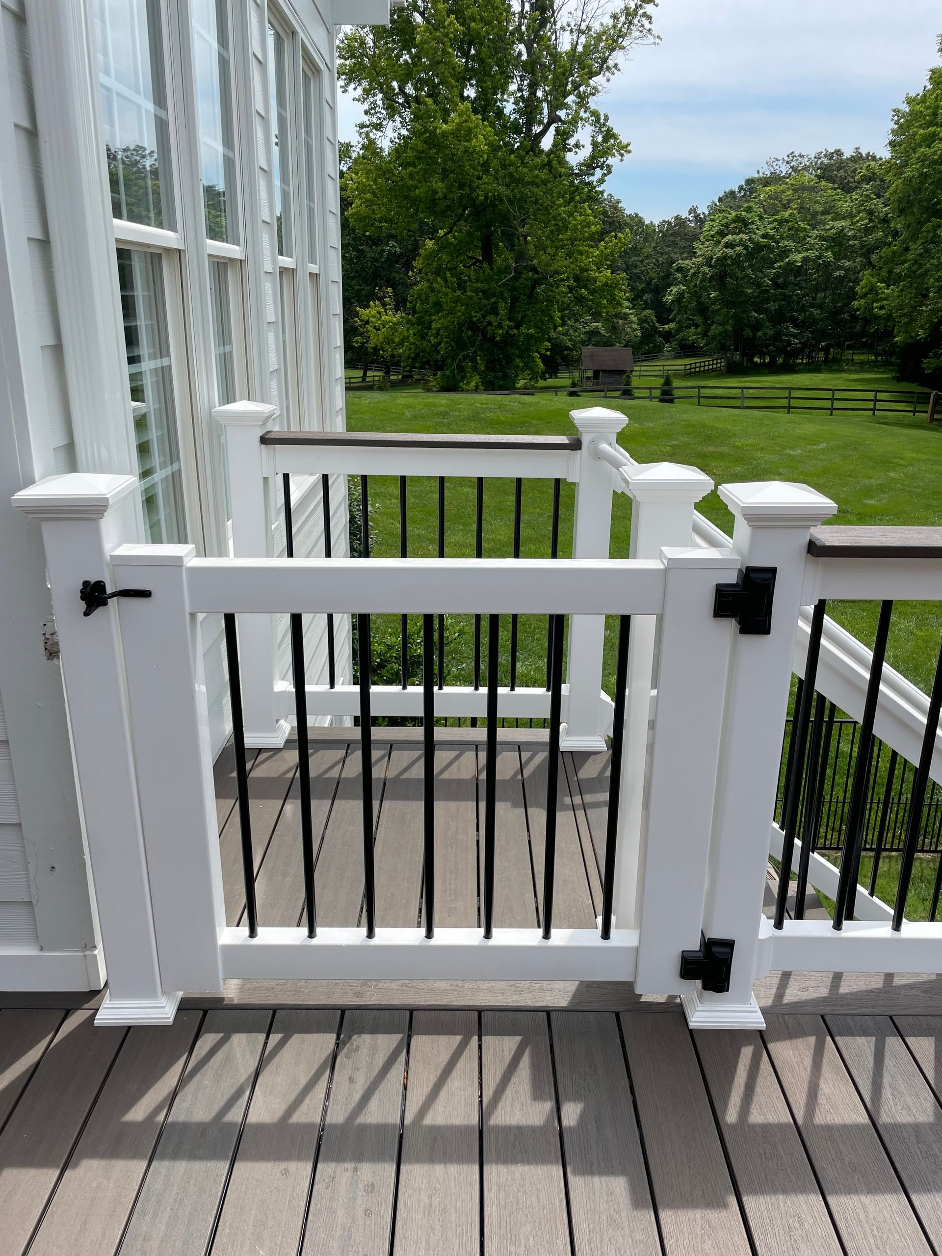 White porch gate with black hinges, opening to a grassy yard beside a glass-walled house.