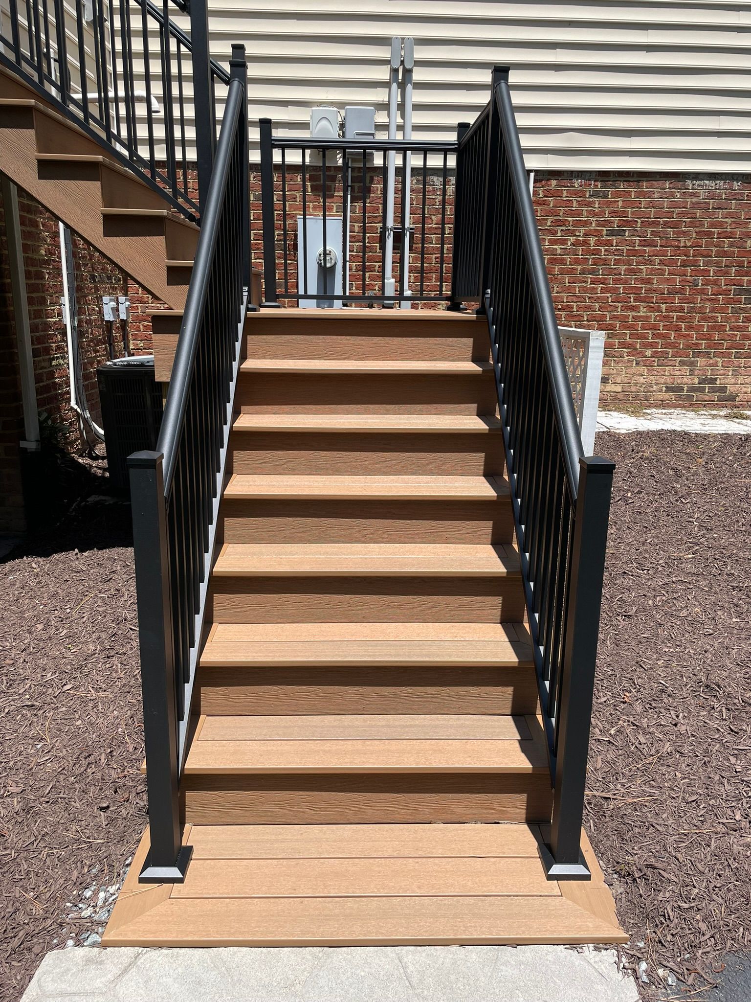 Outdoor wooden staircase with black railings leading up to a brick building entrance