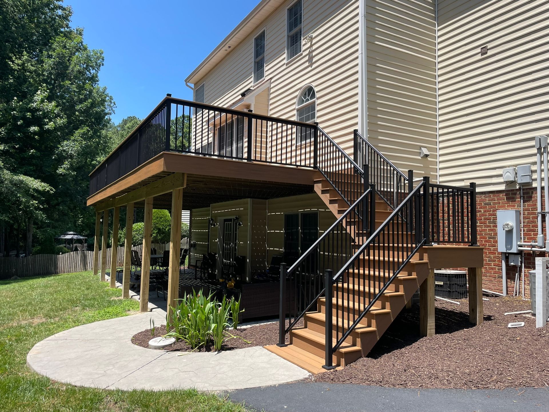 Back deck and staircase on a beige house with black railings, under a wooden deck over a concrete patio.
