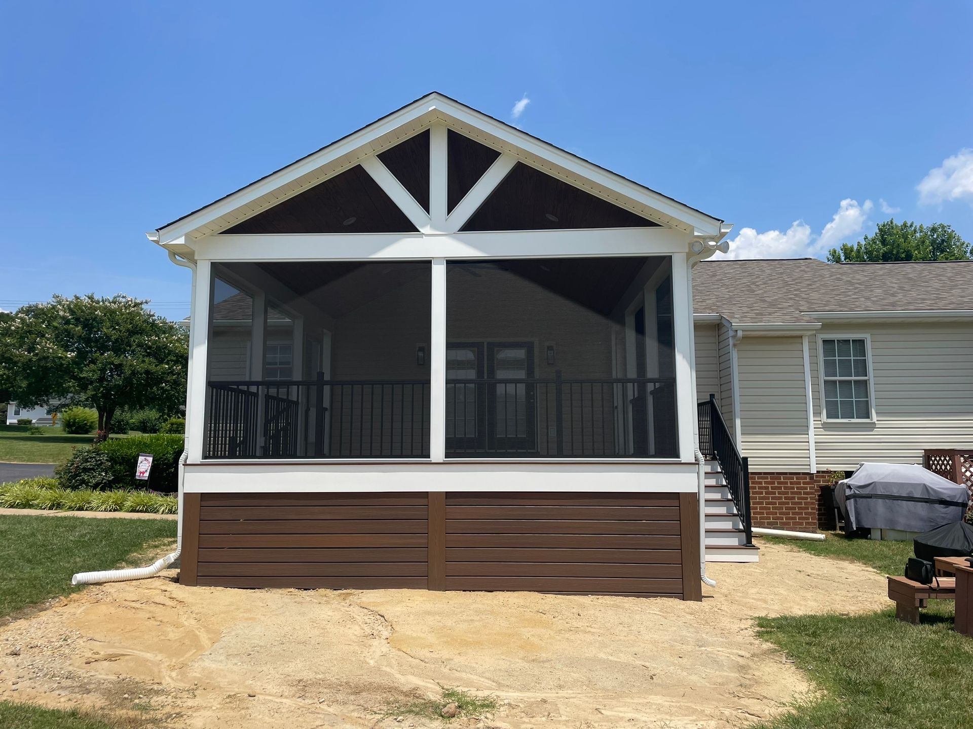 Front porch addition with white trim and brown skirting on a beige house under a blue sky