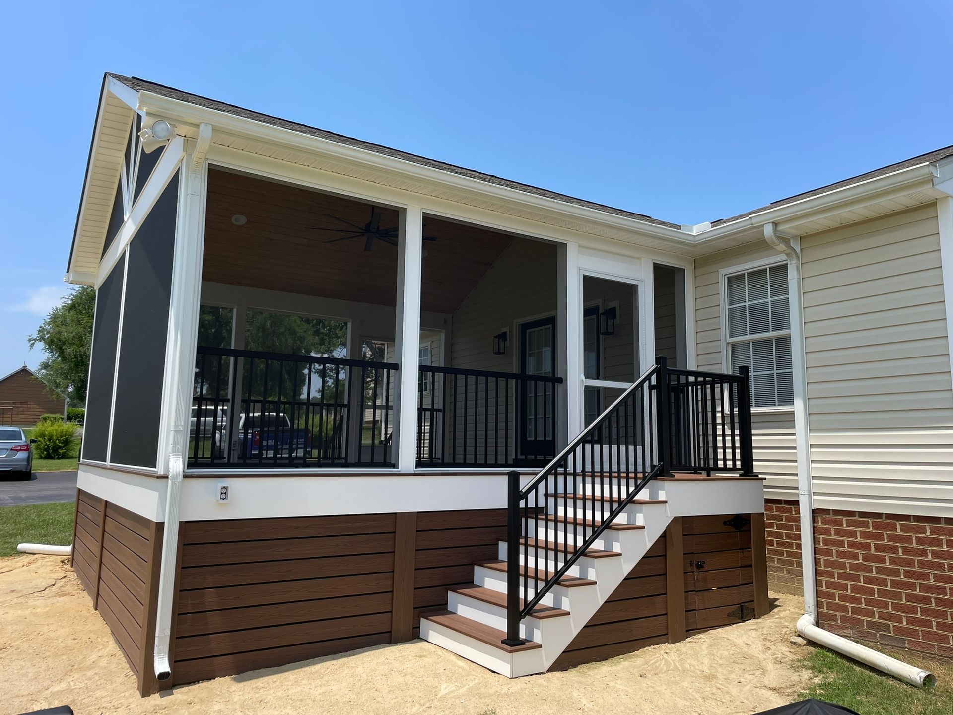 Front porch with black railings and stairs on a beige house with brown skirting and screened seating area