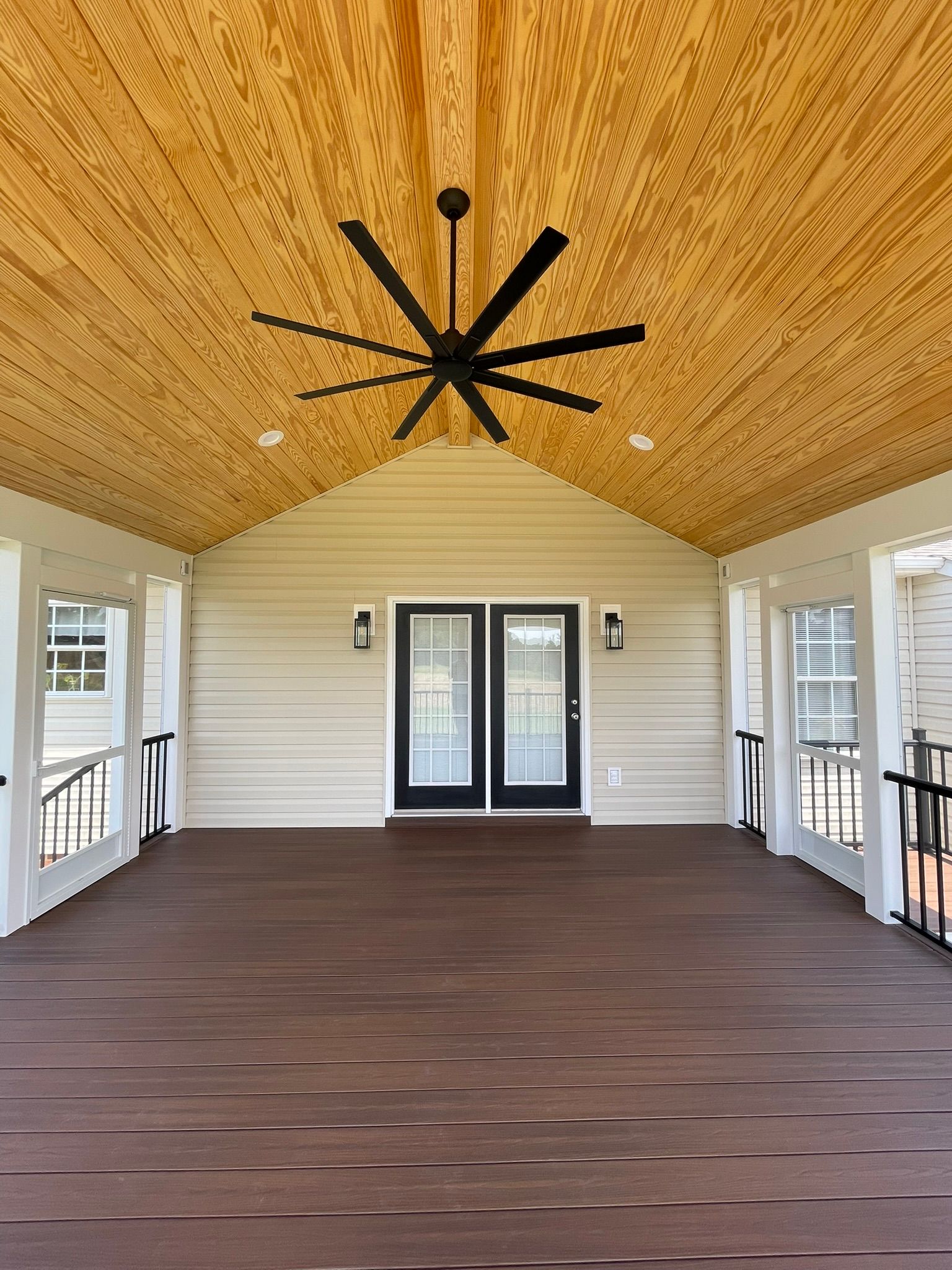 Covered porch with white siding, dark wood floor, and a large ceiling fan under a wood-paneled ceiling