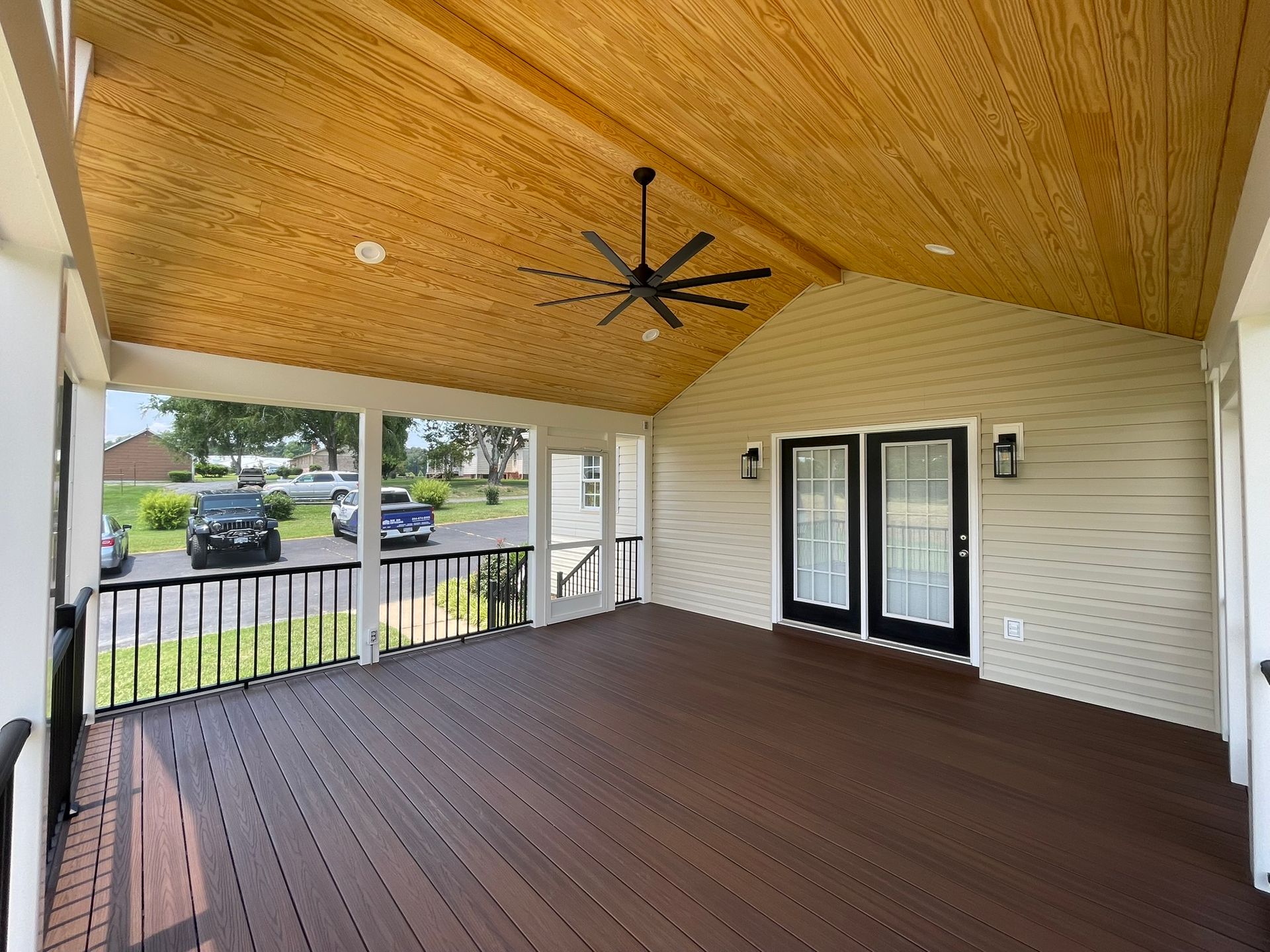 Covered wooden porch with ceiling fan, railings, and double doors on a house.
