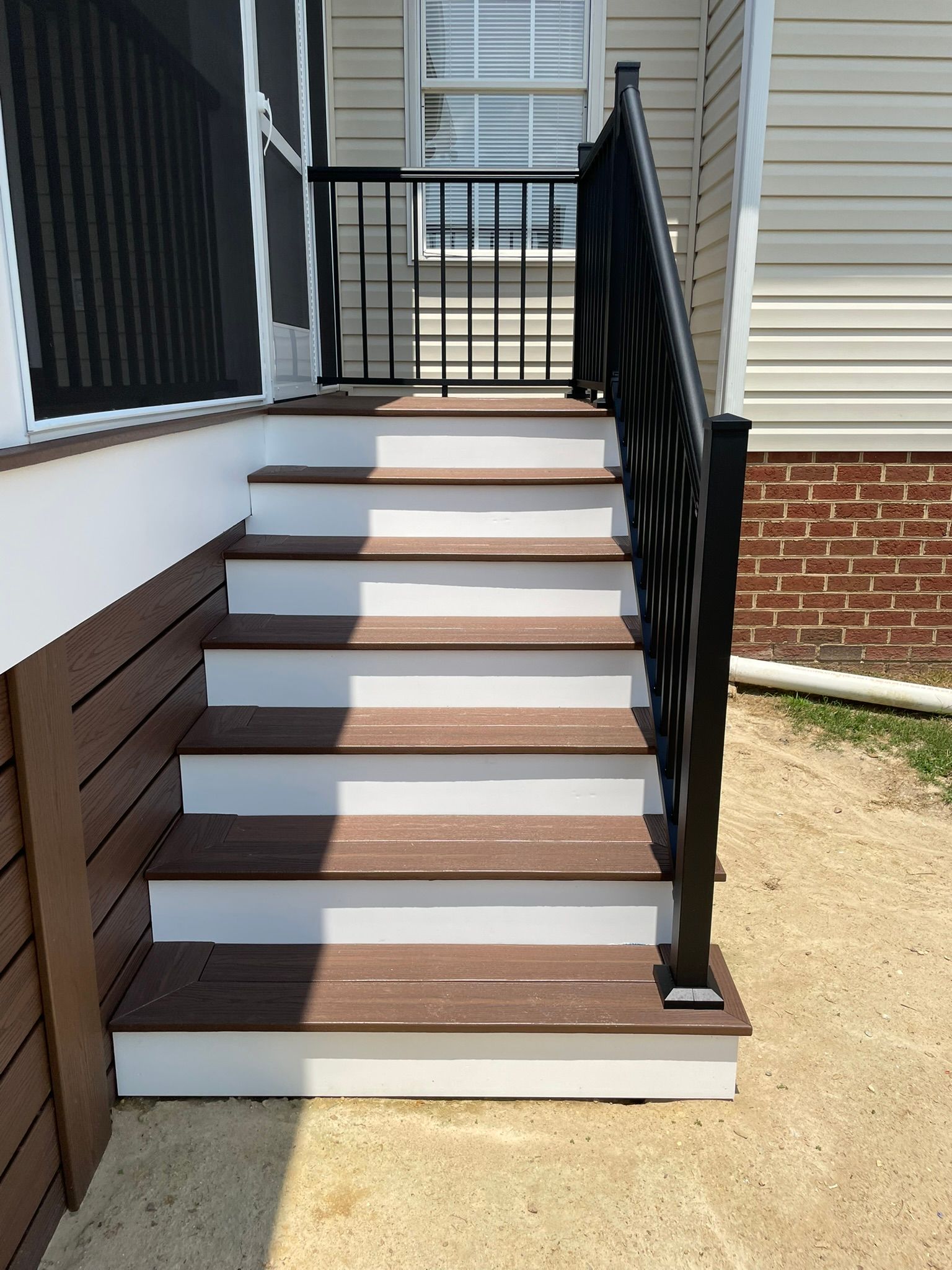 Front steps with white risers and brown treads leading to a porch, with black railings and siding.
