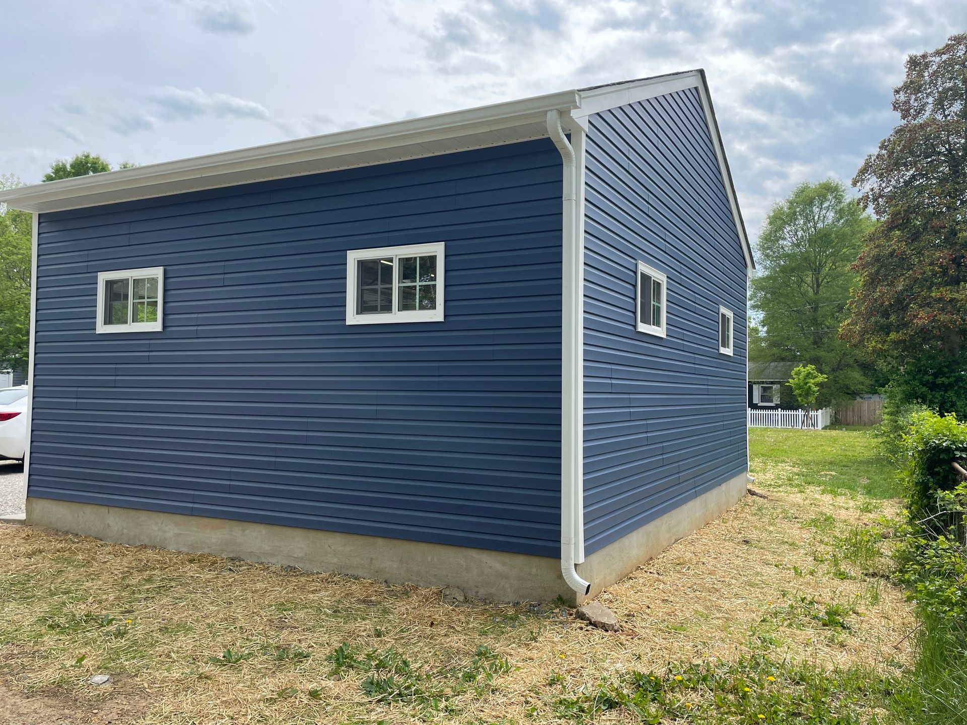 Blue siding on a small building with white trim, viewed from the side in a grassy area.