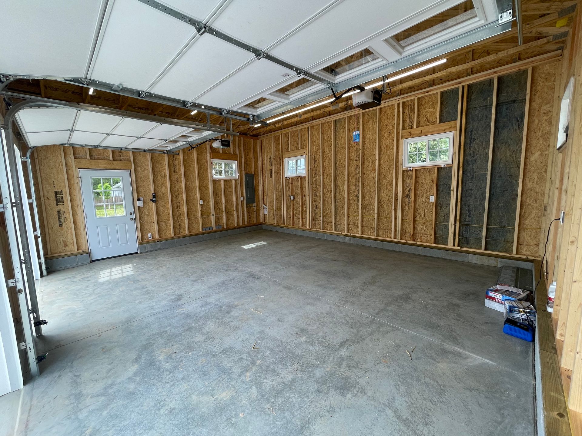 Empty unfinished garage interior with exposed studs, concrete floor, and a white door on the left