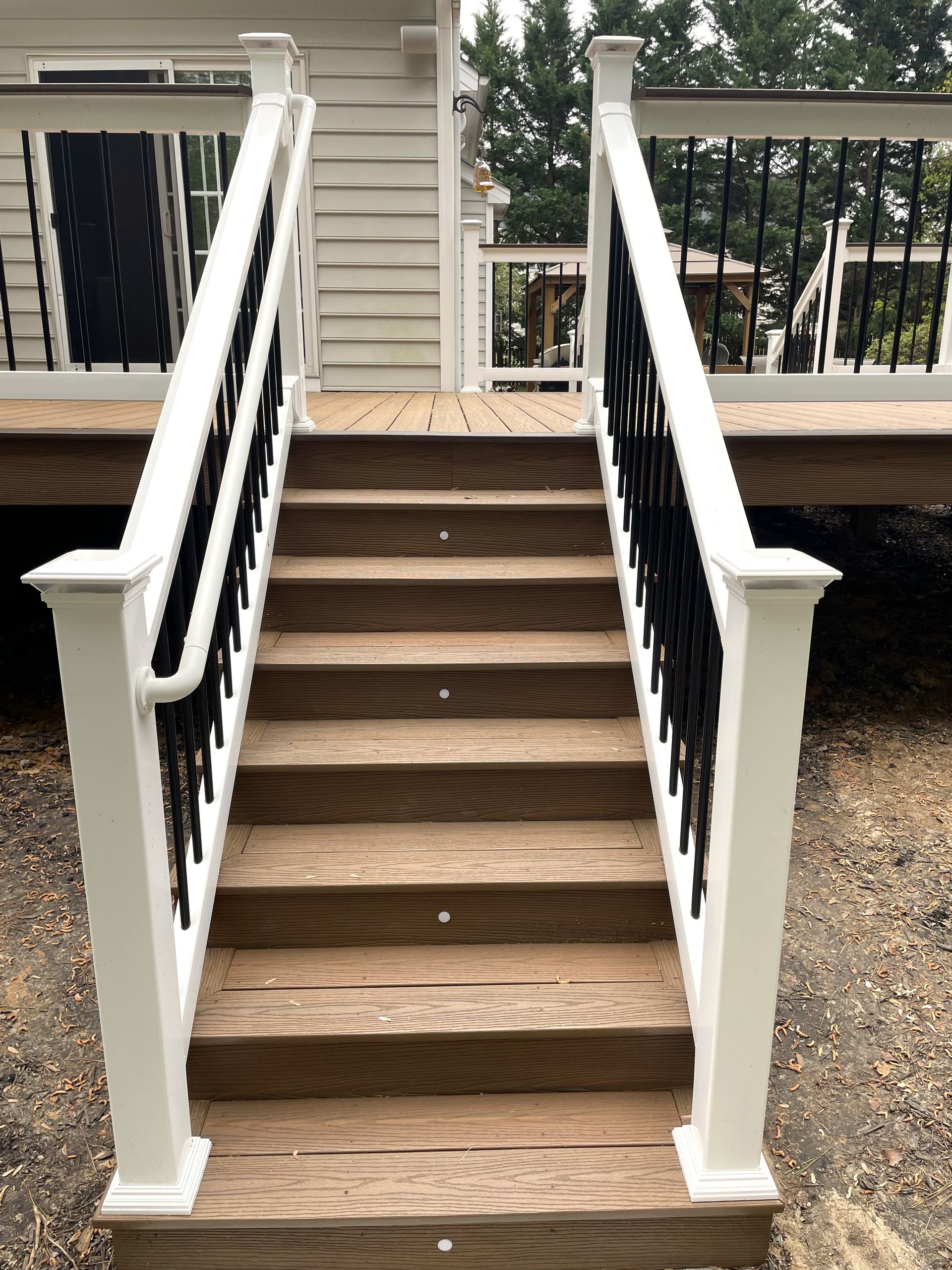 Front porch wooden steps with black railings and white posts leading to a house entrance