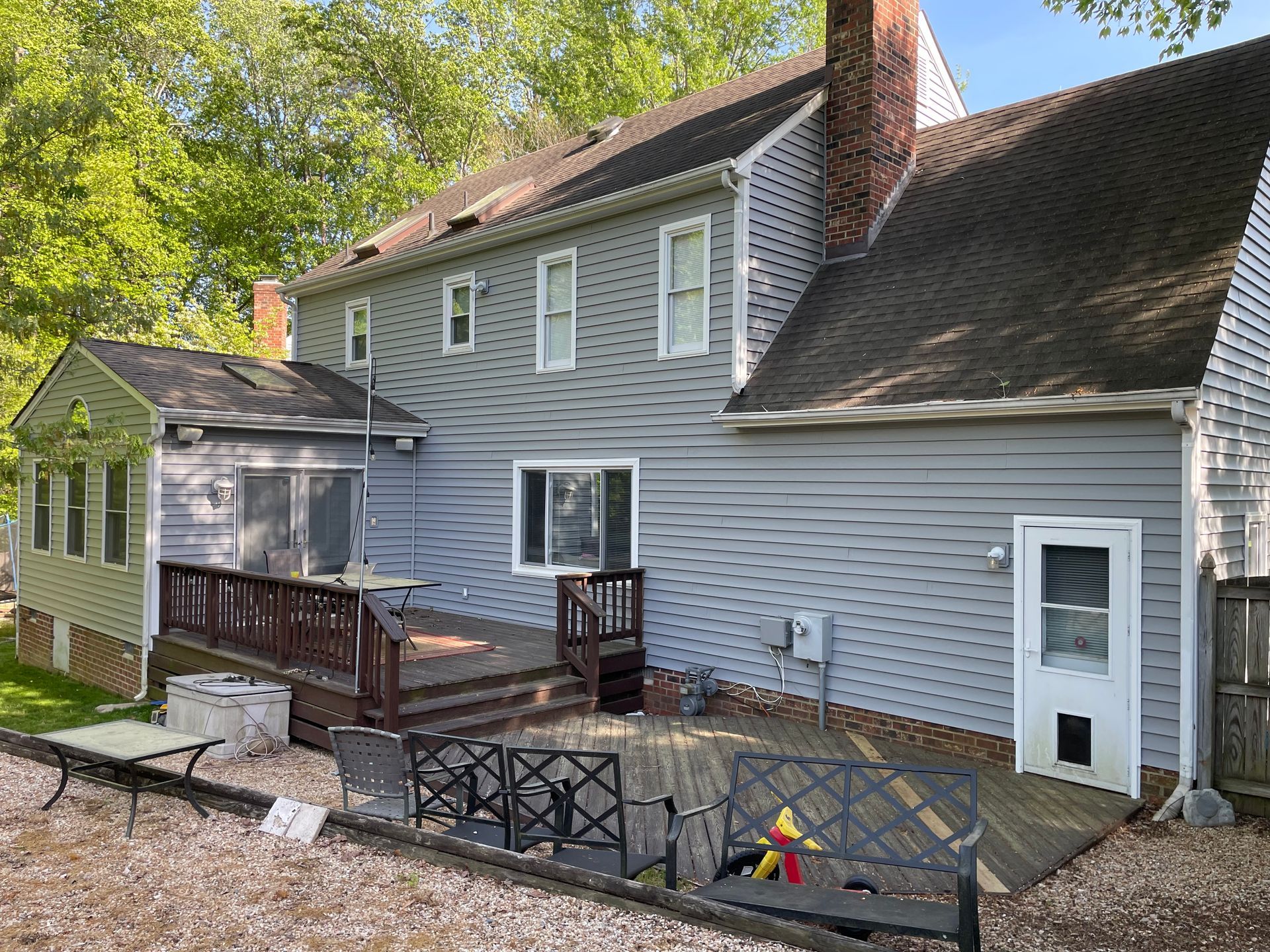 Gray house with white trim and wooden deck, fenced front yard, and a small attached side shed