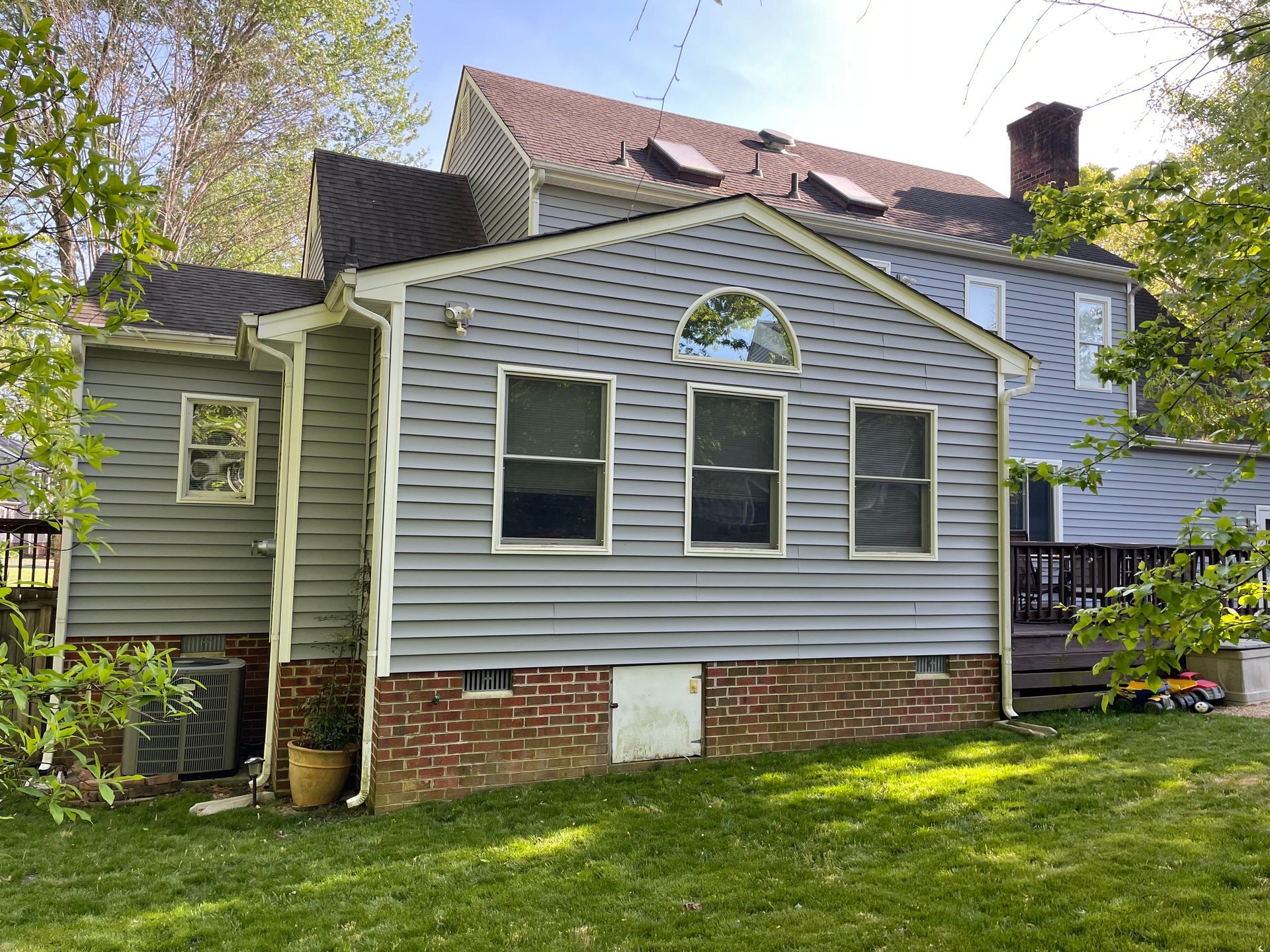 Small gray house with white trim and brick foundation, viewed from the backyard on a sunny day.