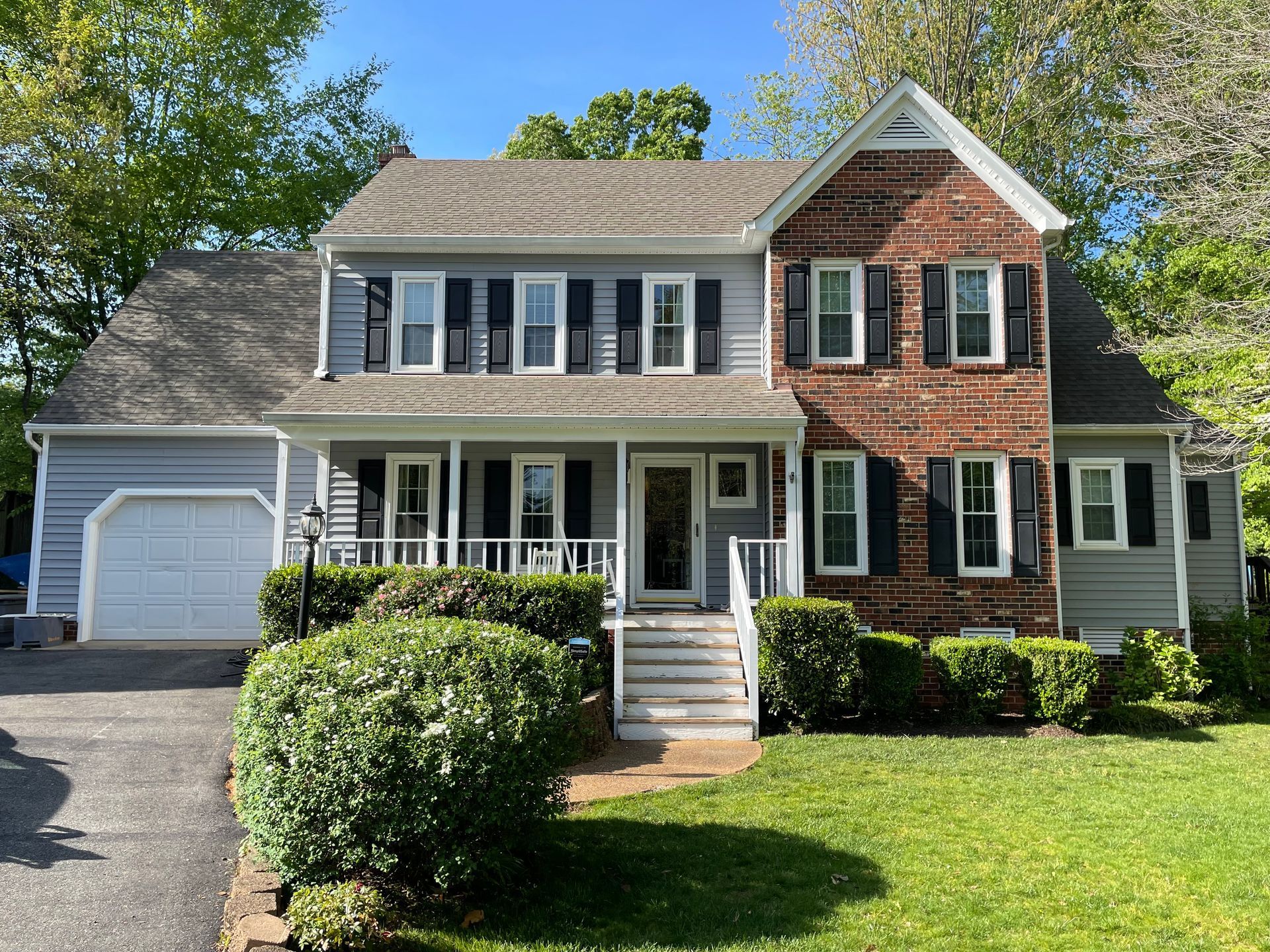 Suburban two-story house with white siding, brick facade, front porch, attached garage, and green lawn