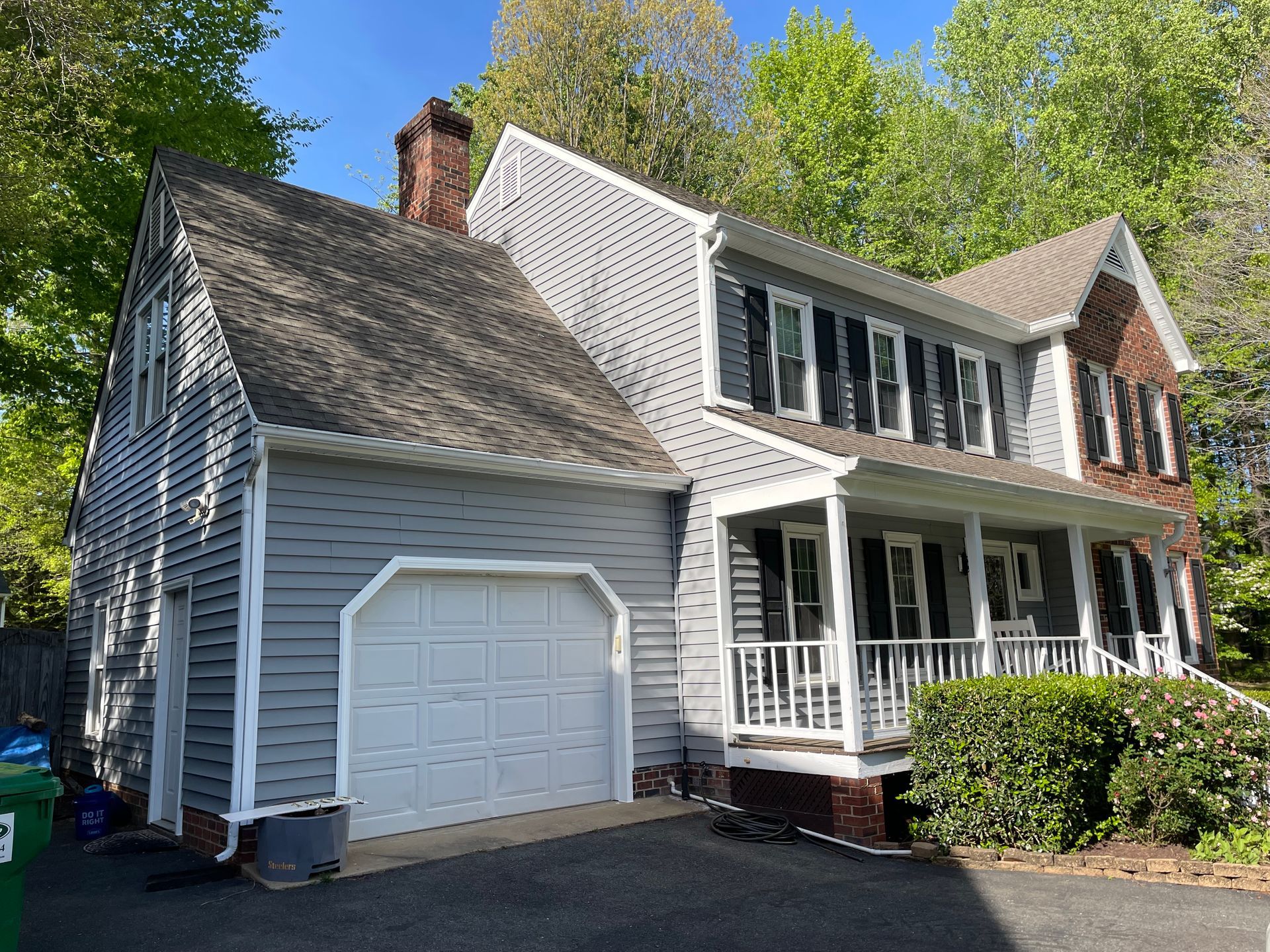 Suburban two-story house with gray siding, white trim, garage, and front porch under trees