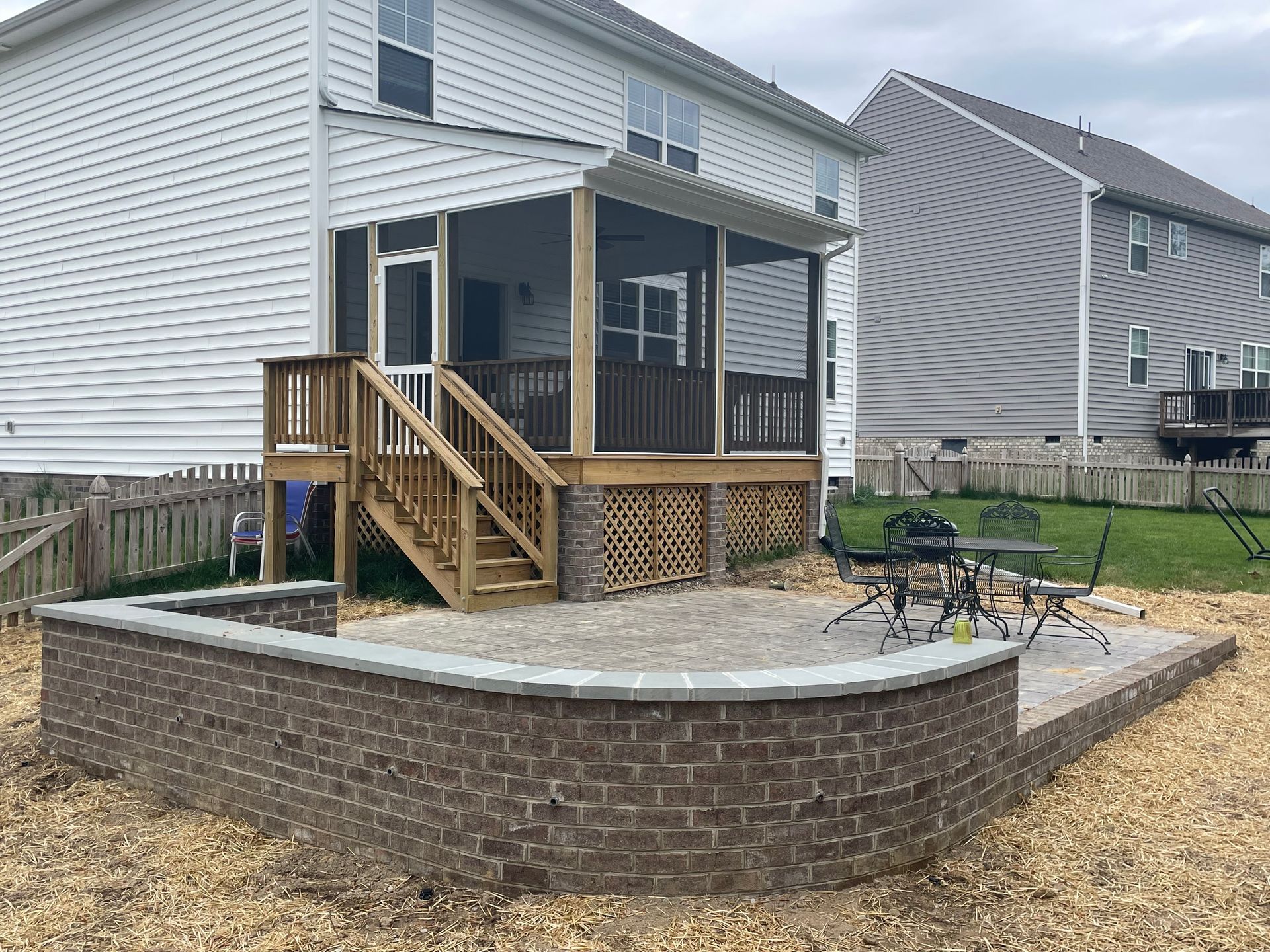 Backyard deck with wooden stairs, brick retaining wall, and patio furniture beside a house