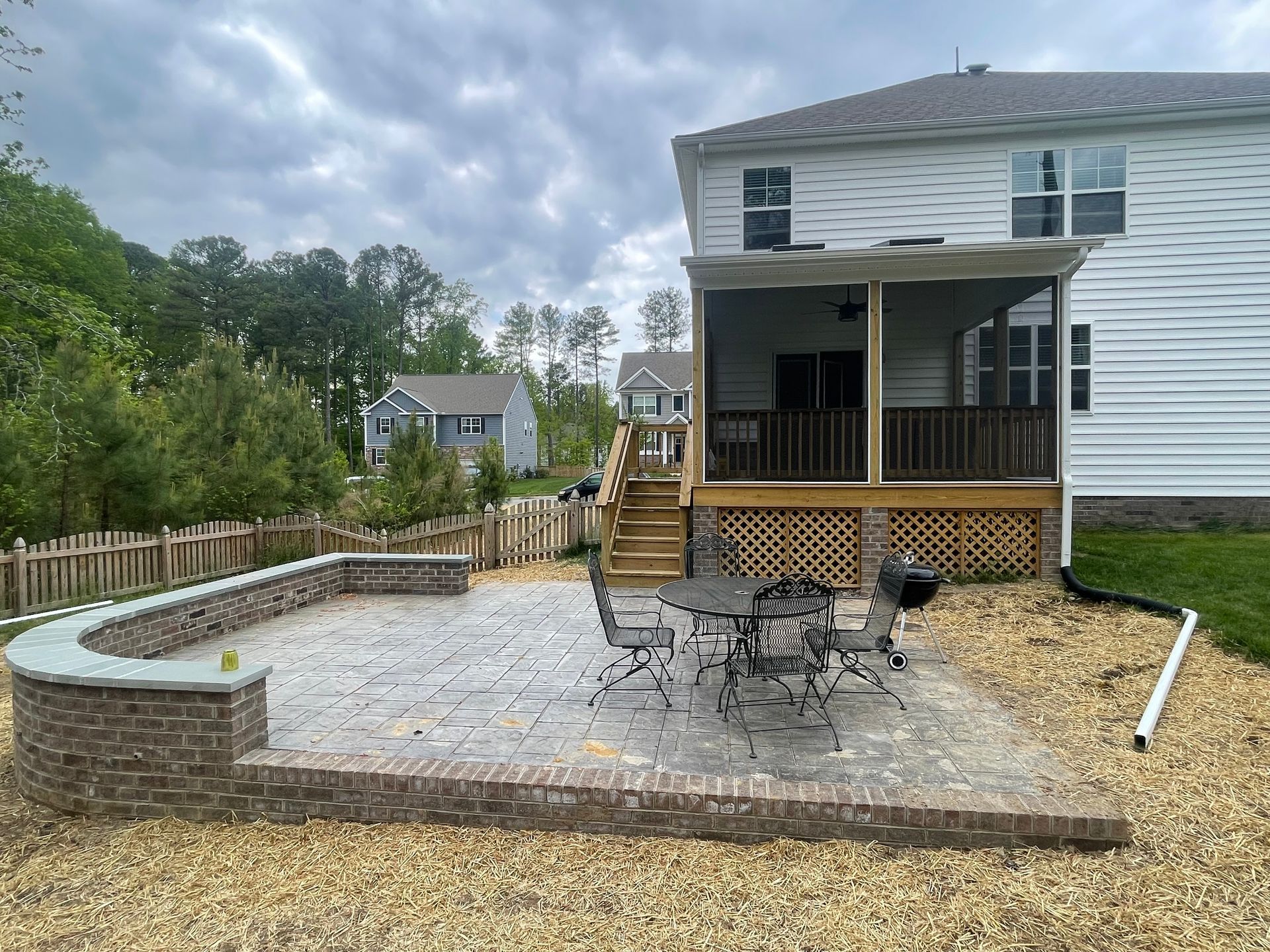 Backyard with raised stone patio, wooden deck, outdoor table and chairs, and a curving retaining wall