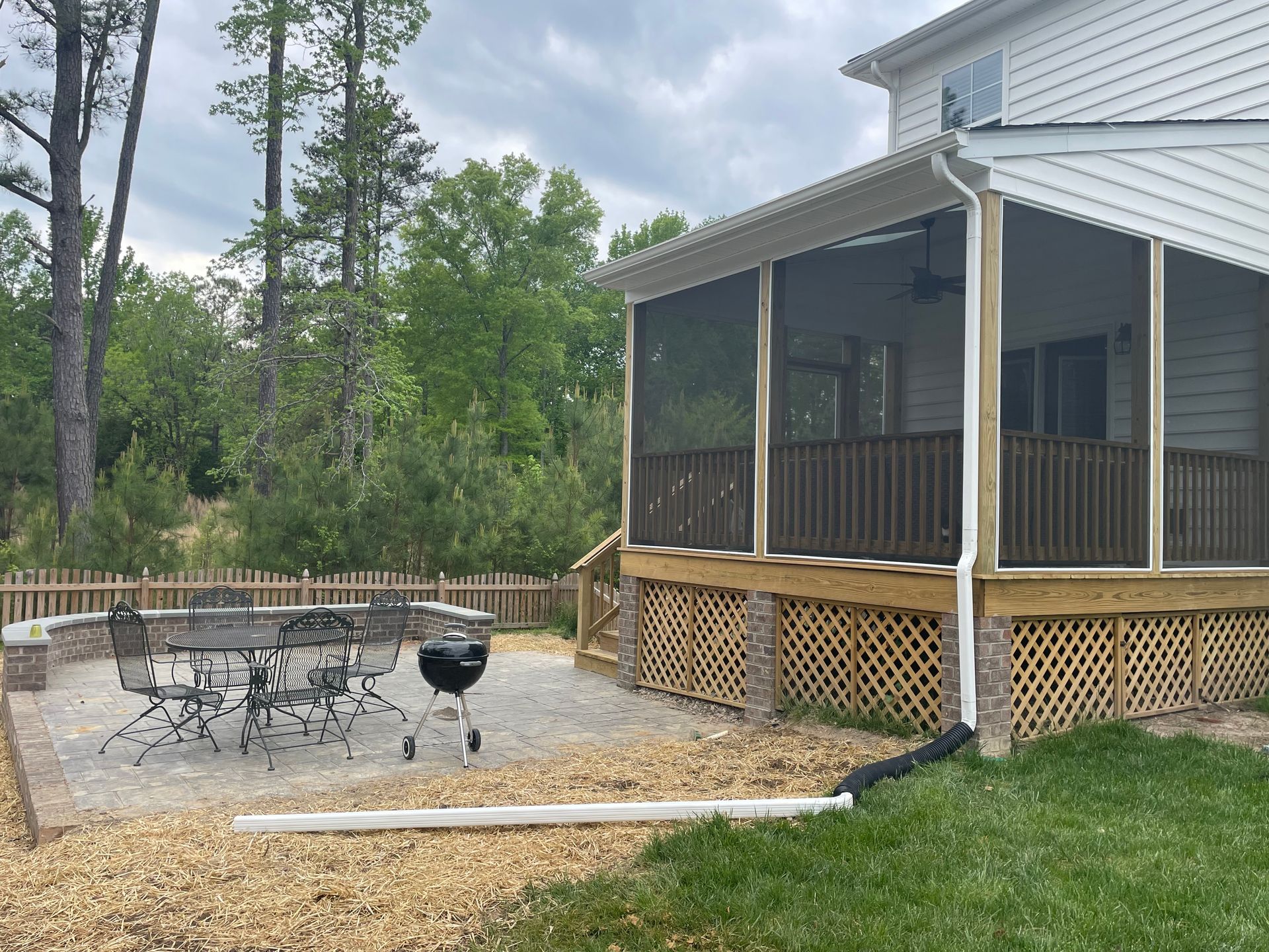 Screened porch with patio table and chairs beside a fenced gravel yard and trees