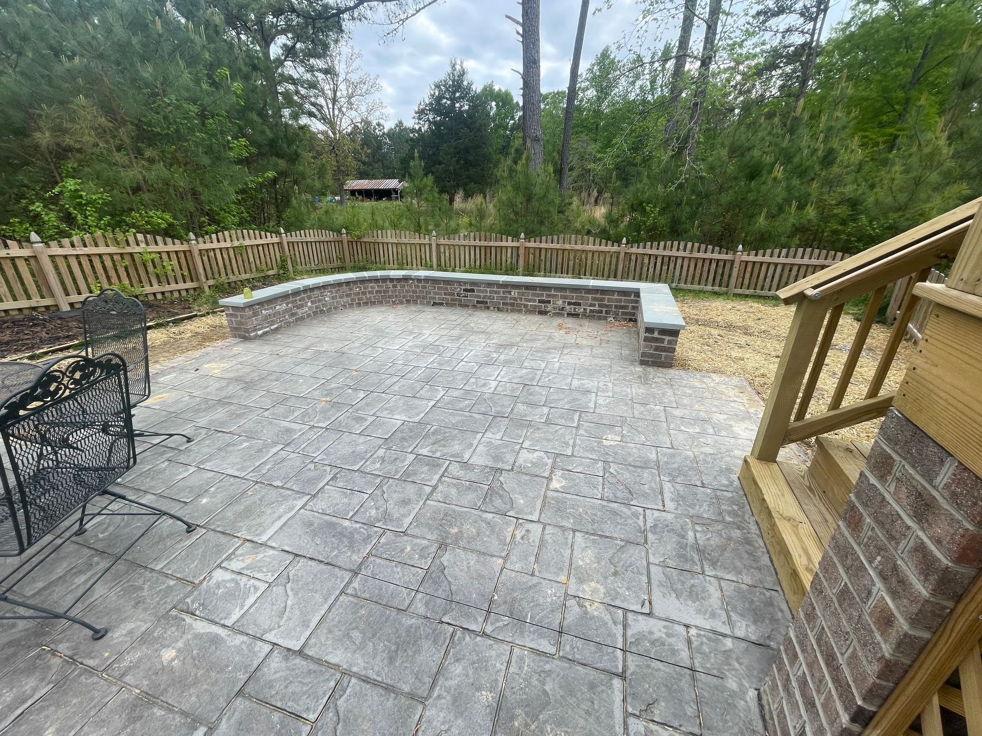 Stone patio with curved retaining wall, wooden fence, and steps overlooking a wooded yard
