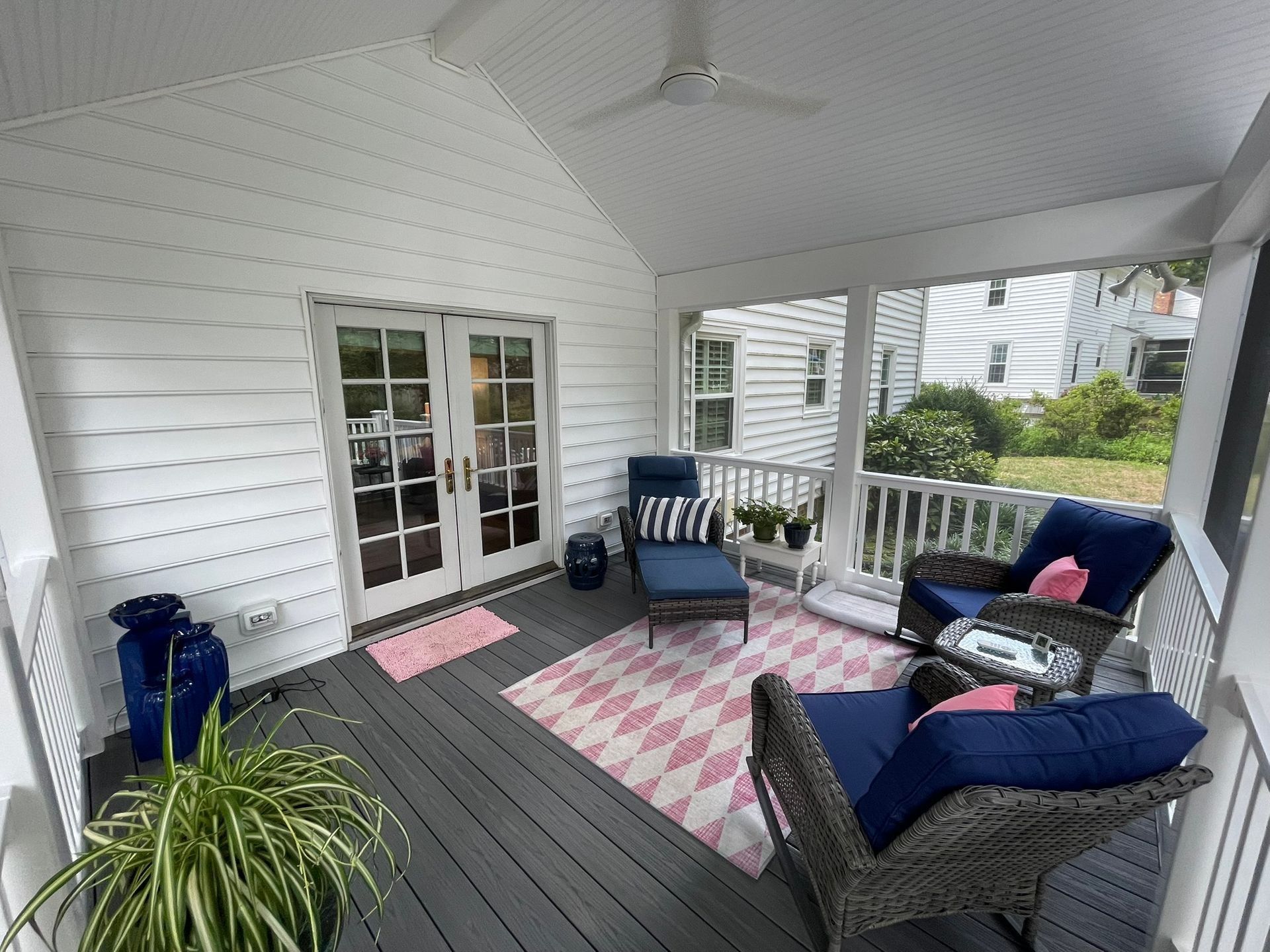 Covered porch with white siding, navy chairs, blue cushions, pink rug, and potted plant