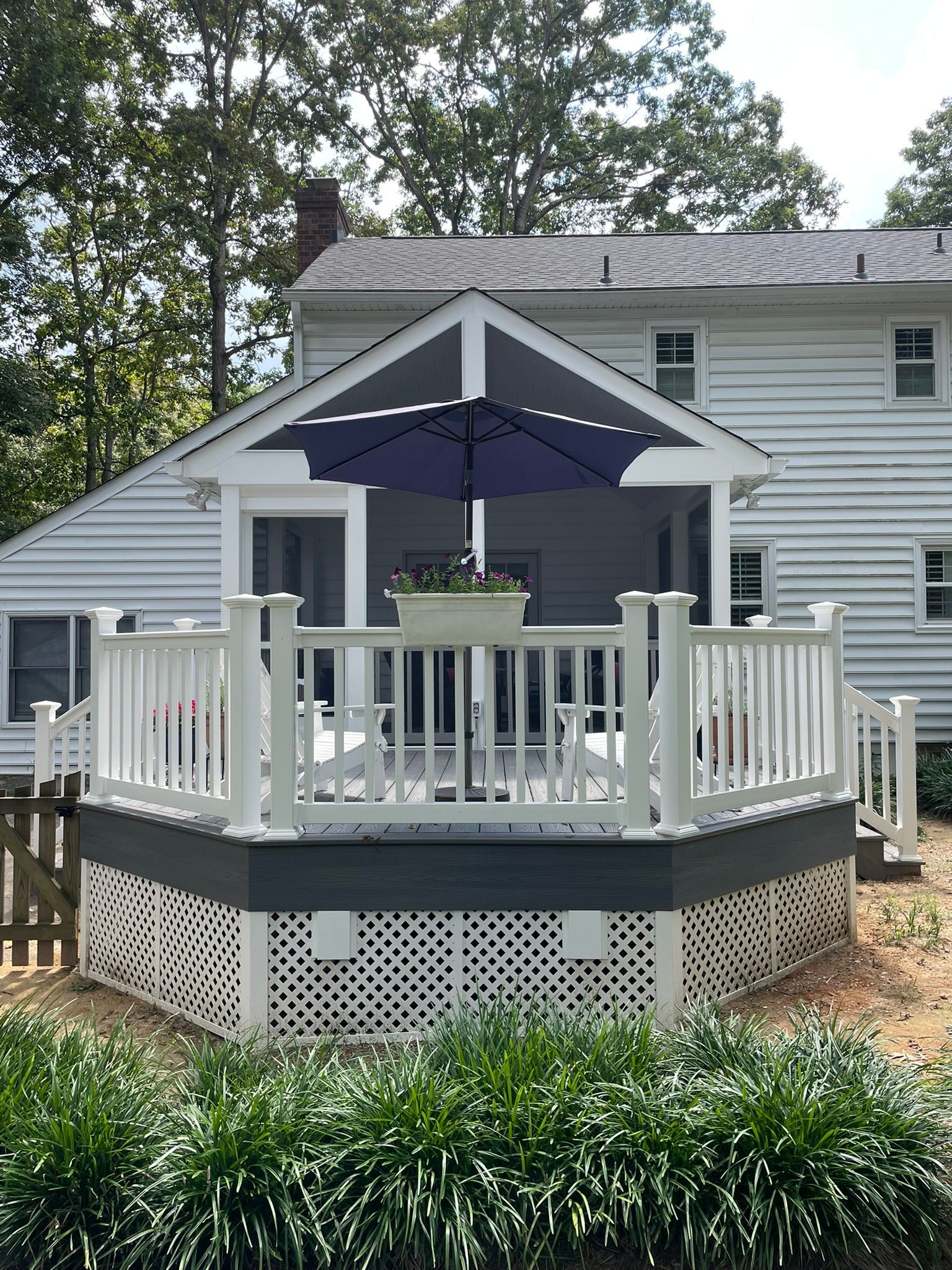 White house deck with railings, dark umbrella, and potted table surrounded by greenery