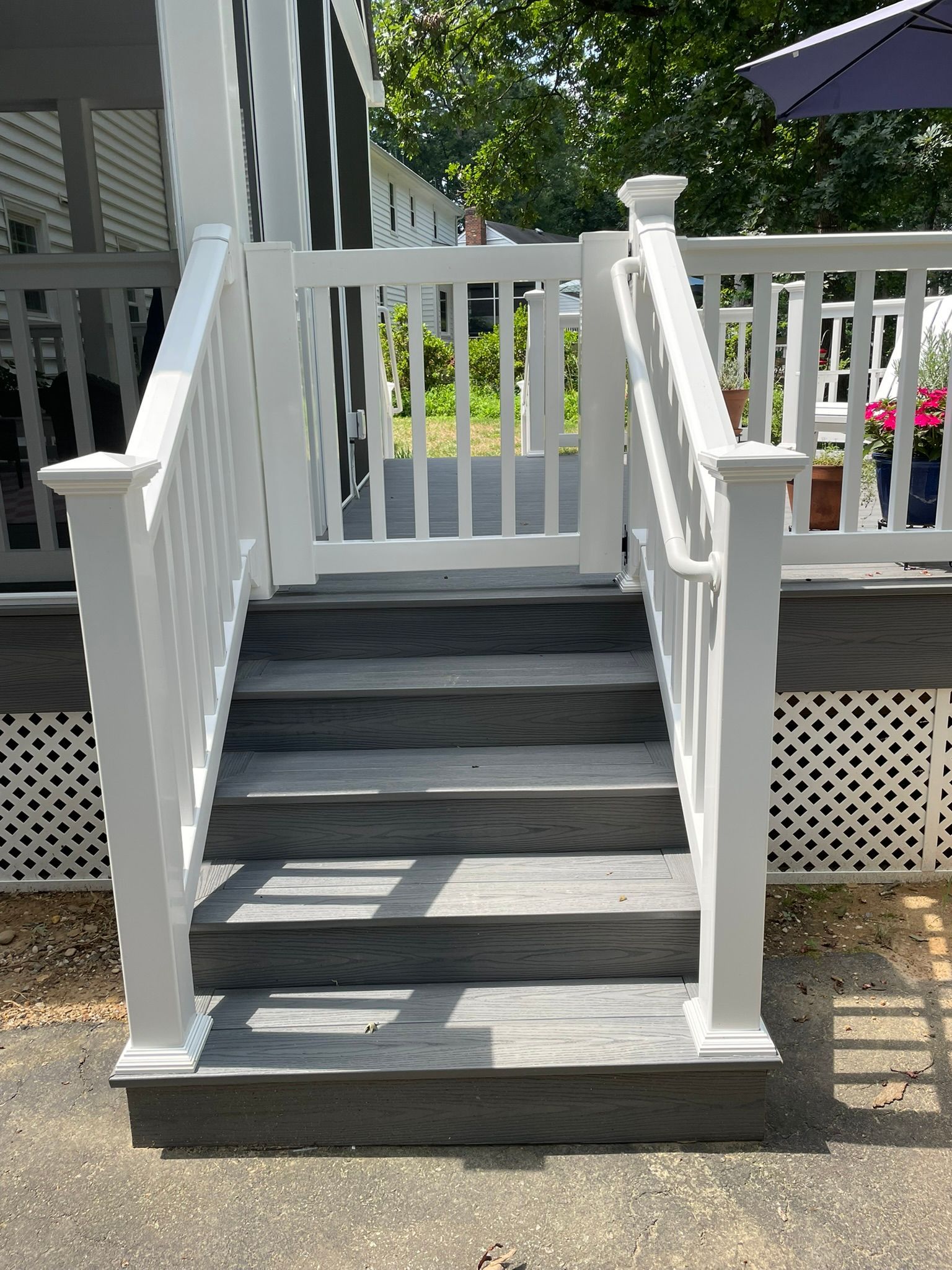 White front porch stairs with railings leading up to a deck, with lattice skirting below.