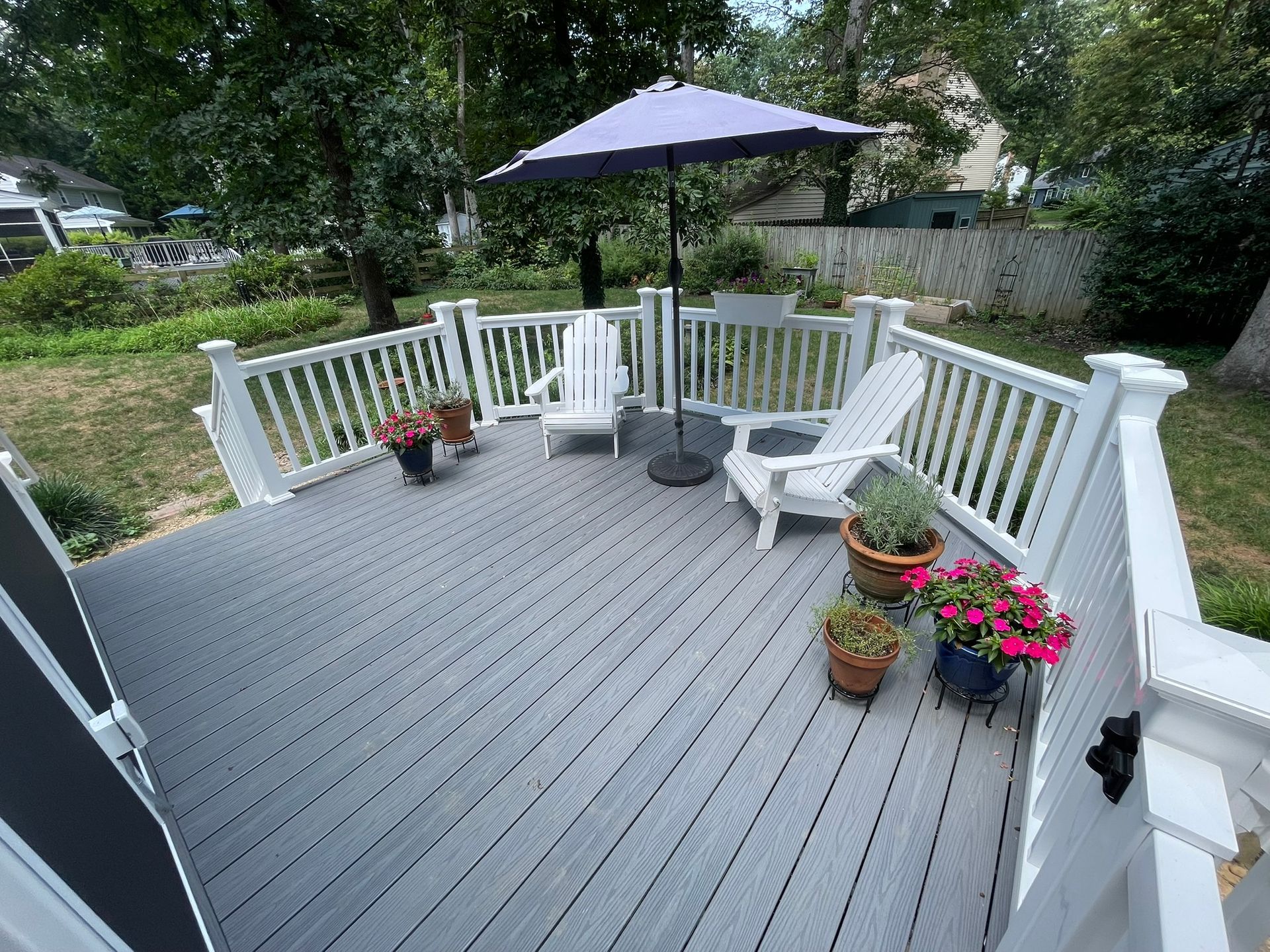 White-railed wooden deck with patio umbrella, chair, and potted flowers overlooking a garden.
