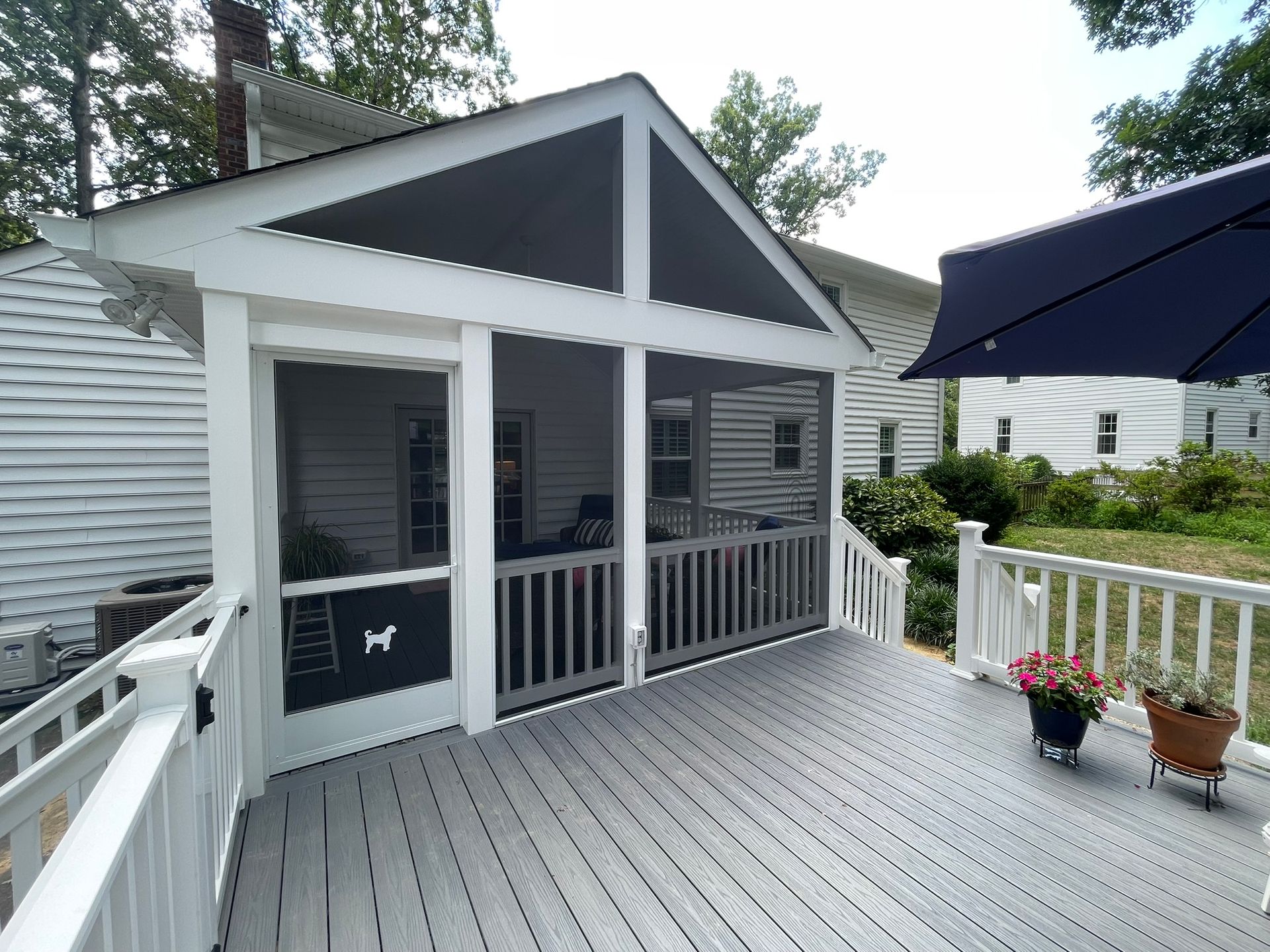 Gray porch deck with white railing, black umbrella, and flower pot beside a small house