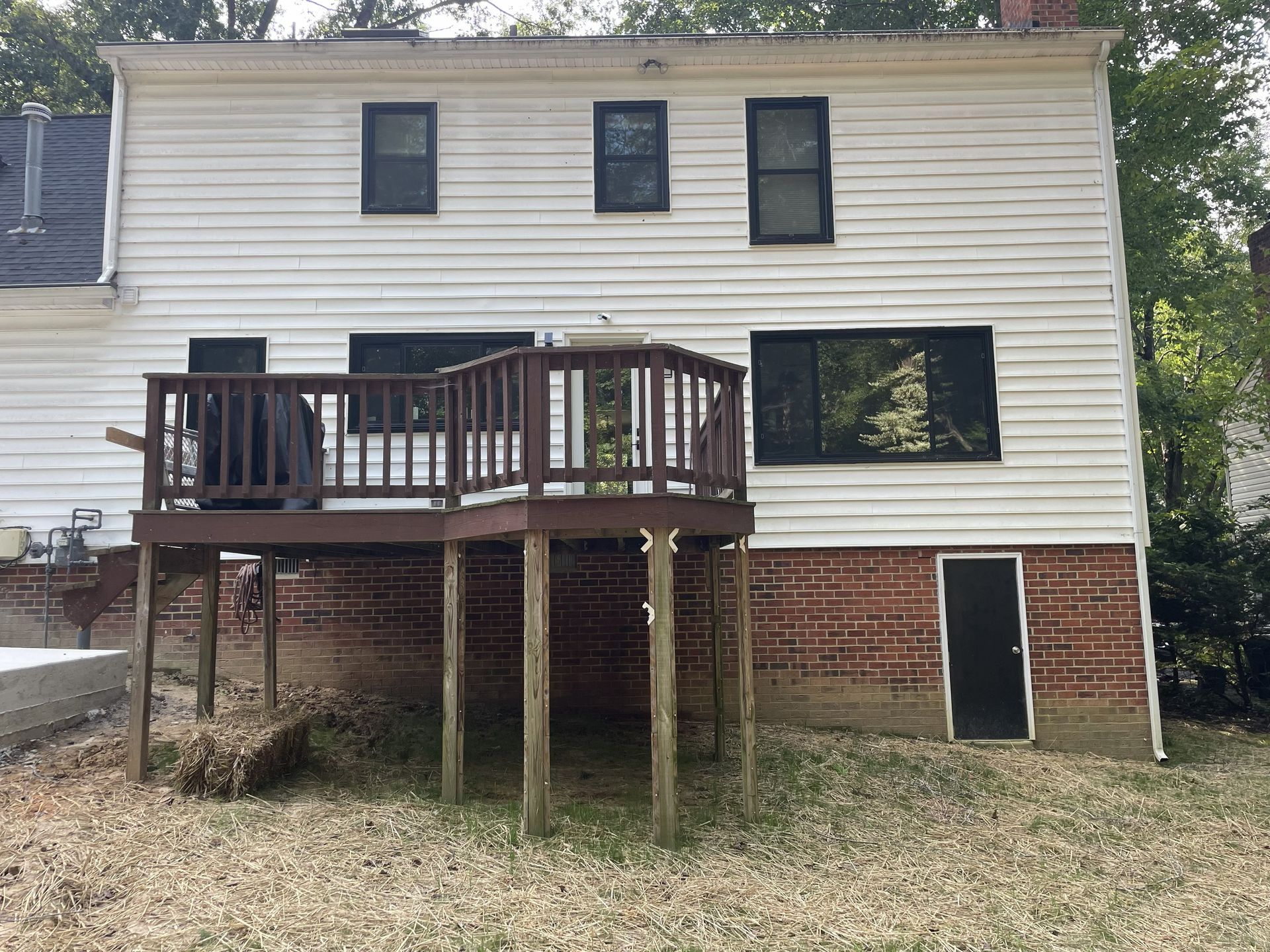 Two-story white house with brick base and elevated wooden deck in a yard