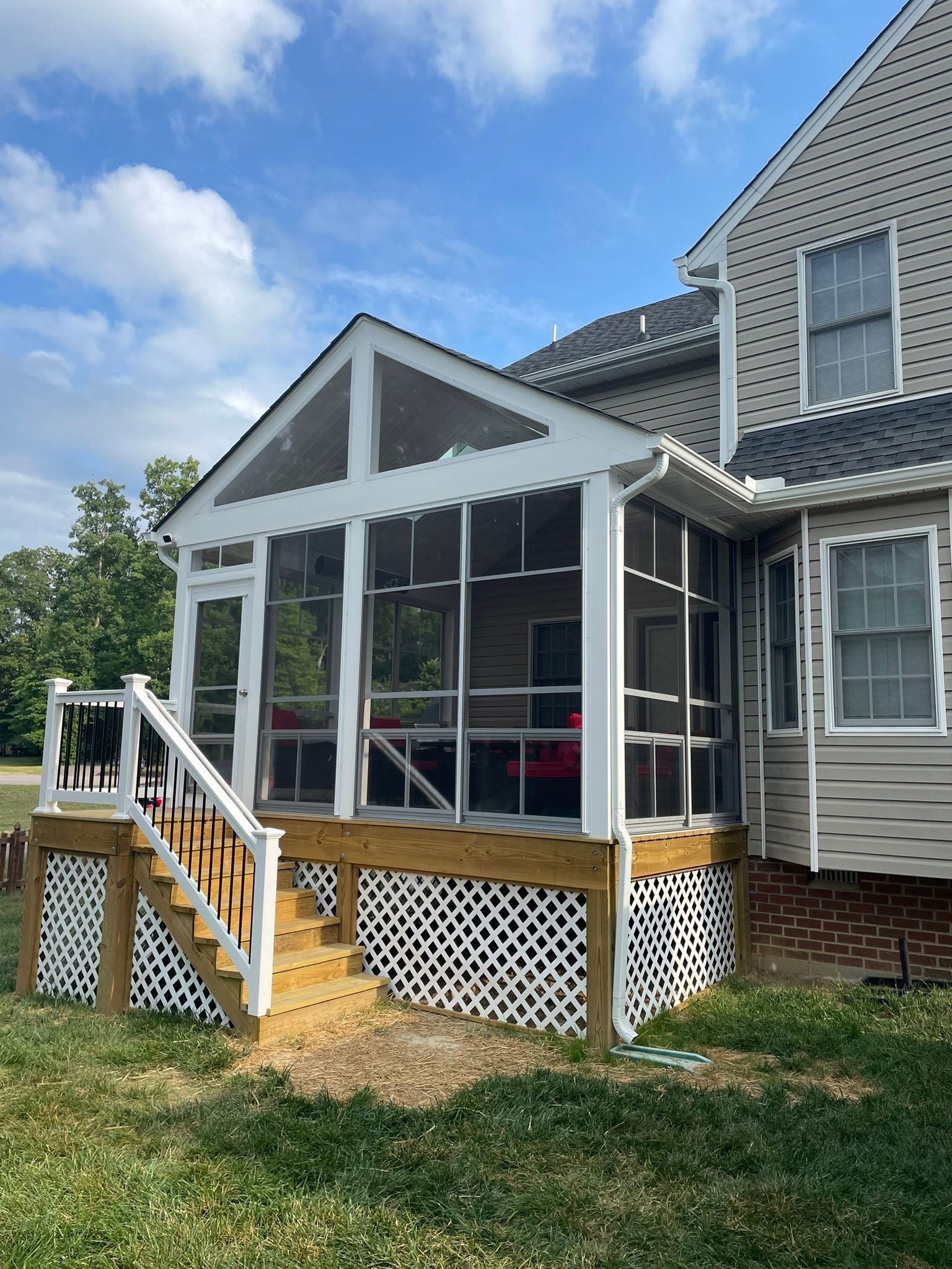 Screened porch with white trim and stairs attached to a gray house on a grassy yard
