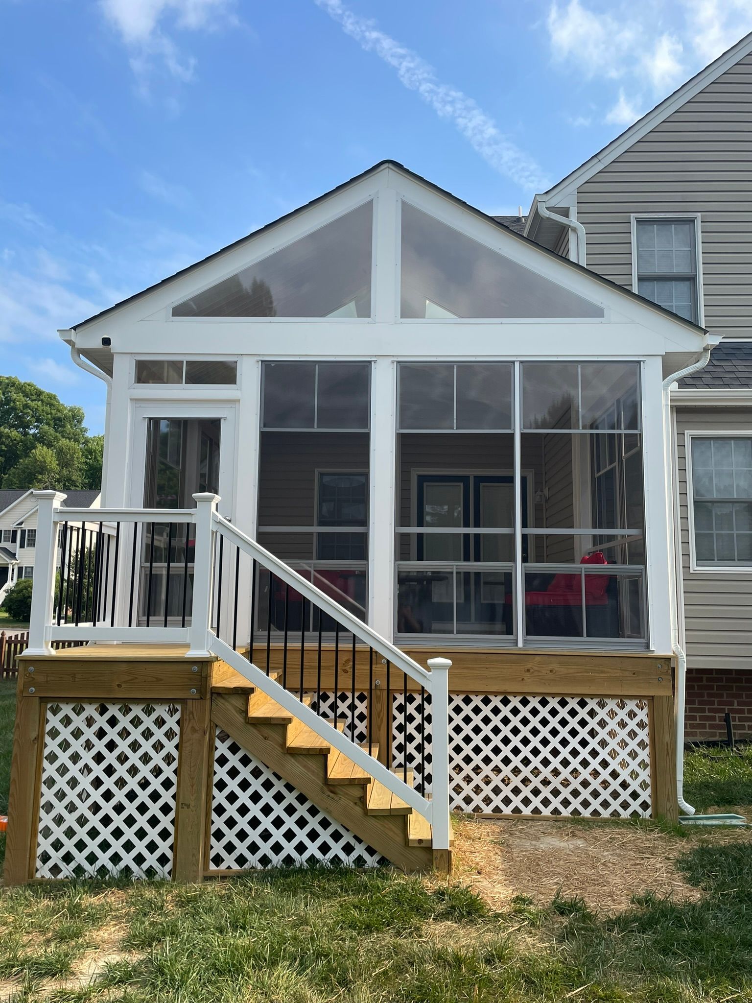 White screened porch with steps, railing, and lattice skirting on a house under a blue sky.