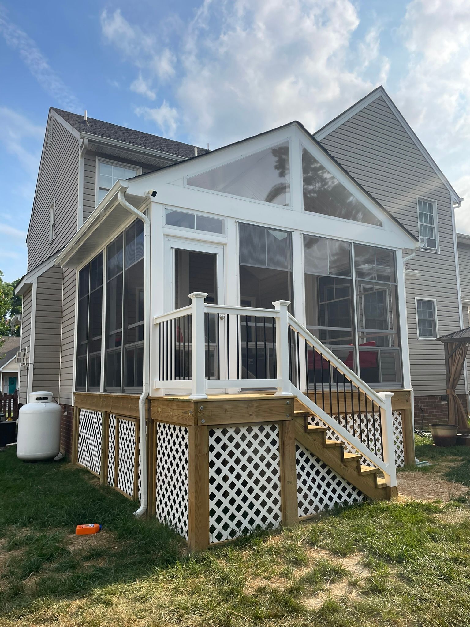 White screened porch with stairs and lattice under a gabled roof on a house