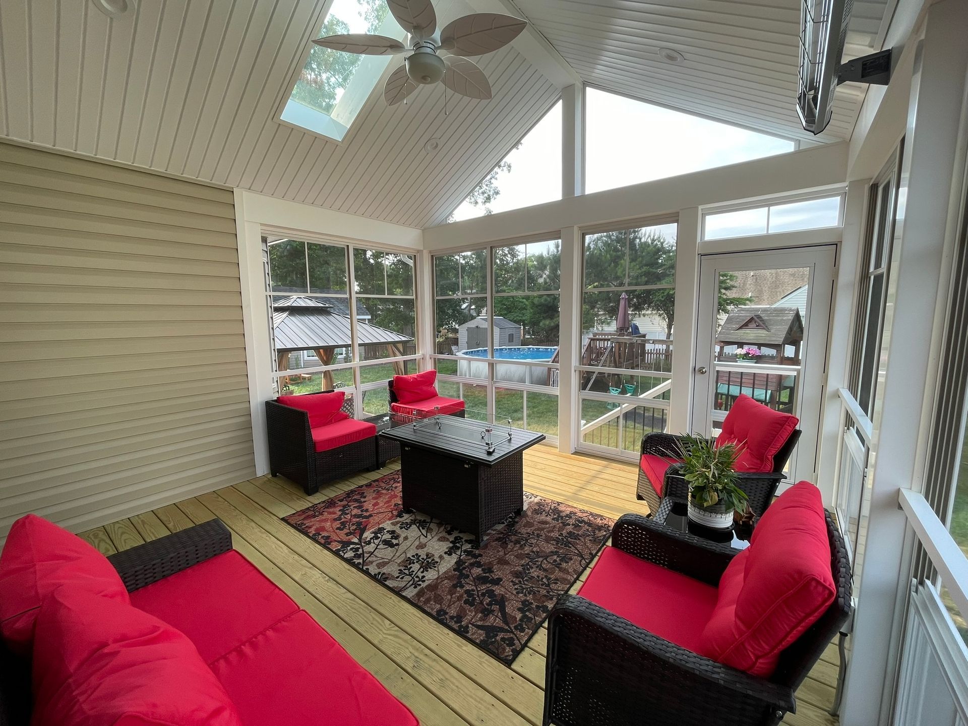 Sunroom with red cushioned chairs, a black coffee table, and large windows overlooking a pool.