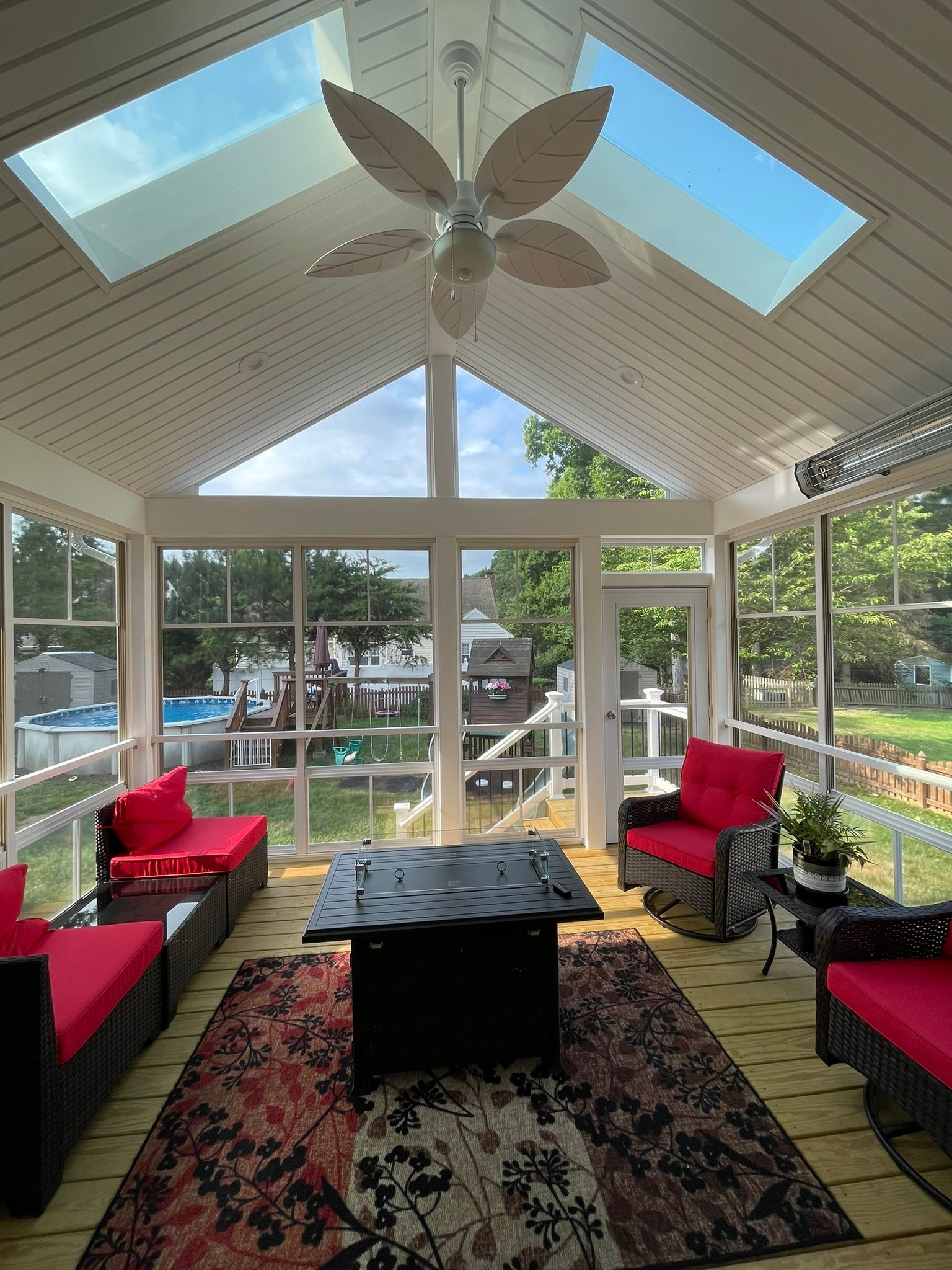 Sunroom with skylights, red chairs, black coffee table, and large windows overlooking a garden and patio.