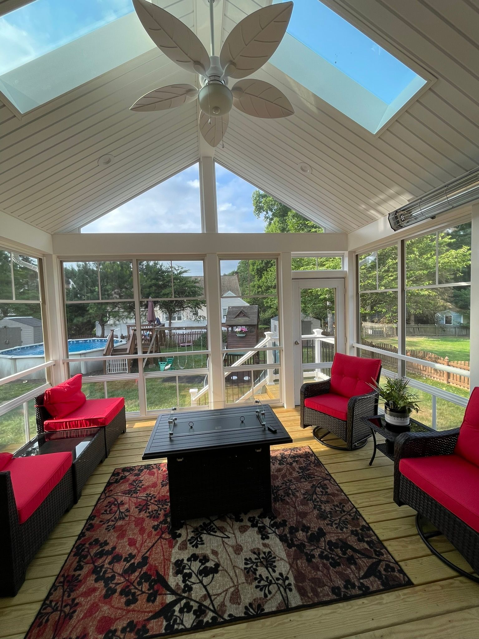 Sunlit screened porch with red cushioned chairs, patterned rug, and a central coffee table under a vaulted ceiling