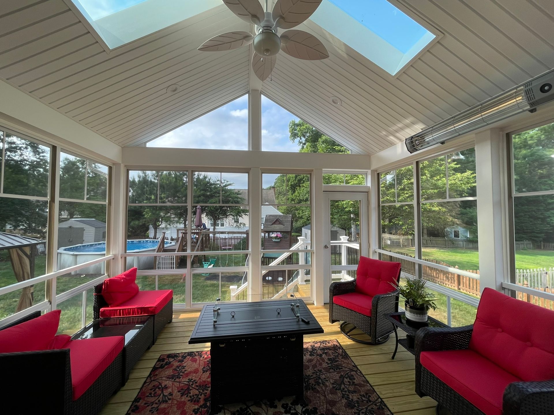 Sunroom with red sofas, black coffee table, ceiling fan, and large windows overlooking greenery