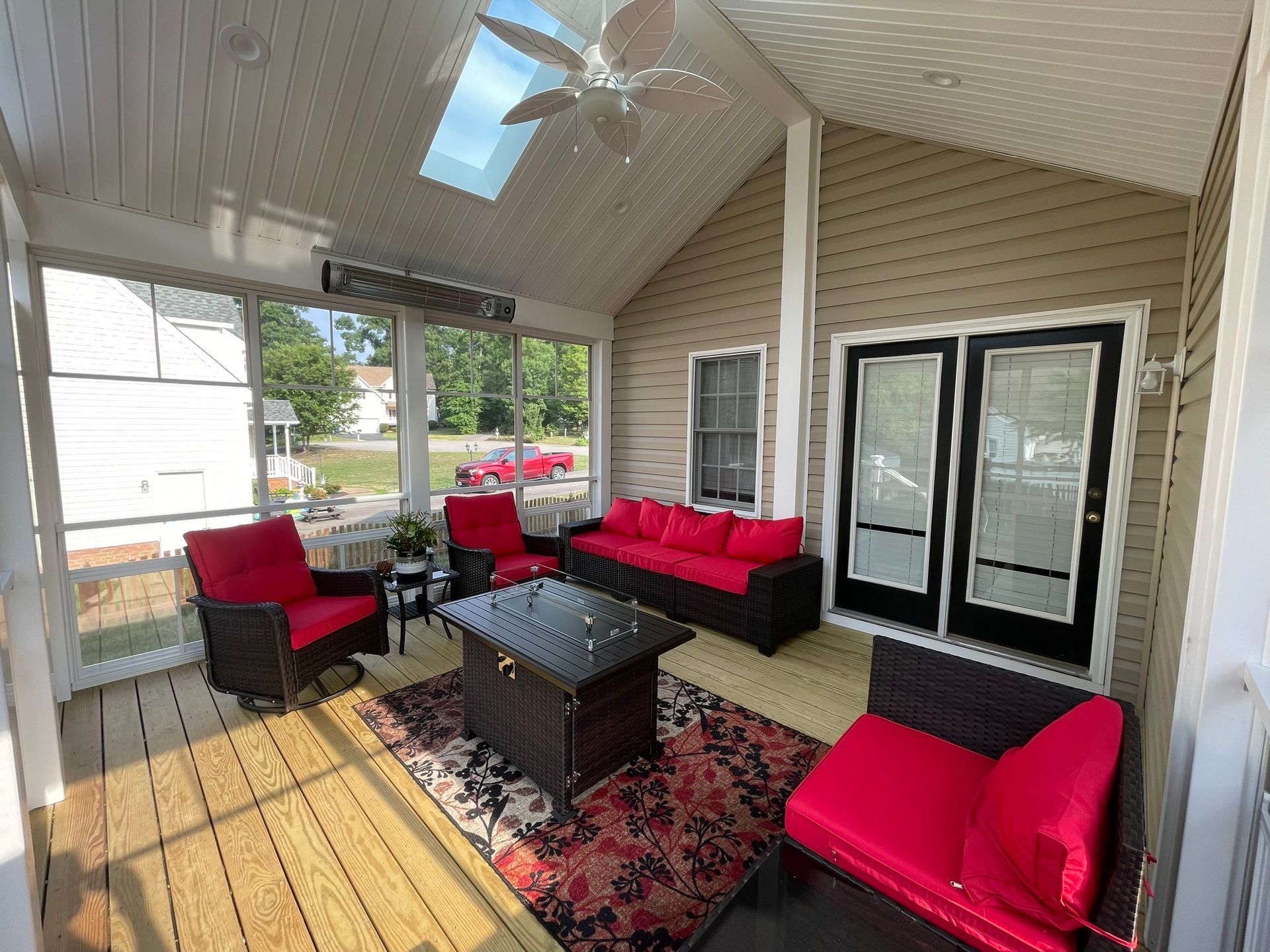 Screened porch with red outdoor seating, black table, patterned rug, and skylight ceiling.