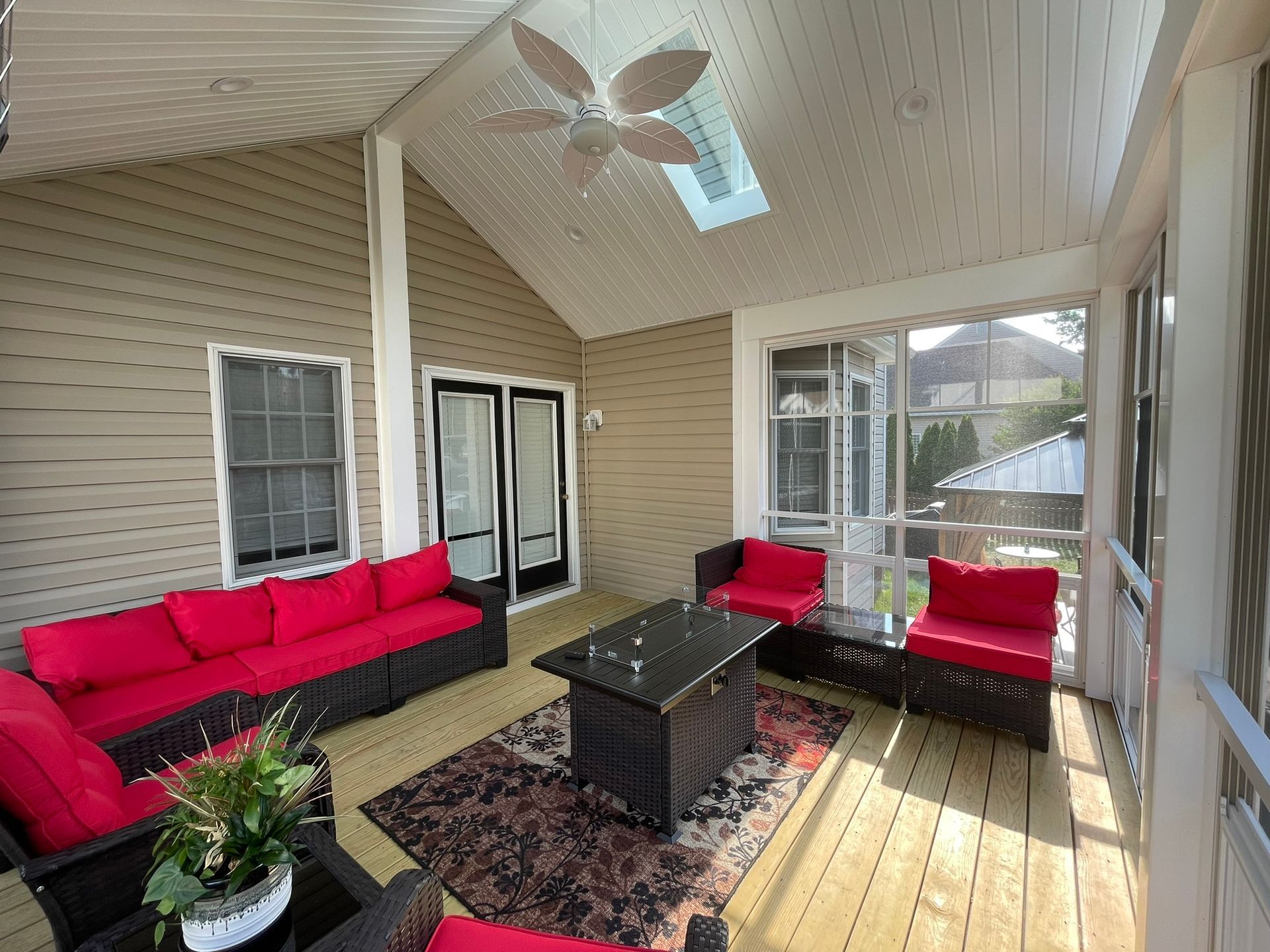 Covered patio with red sofas, black coffee table, and hanging ceiling fan beside a screened window.