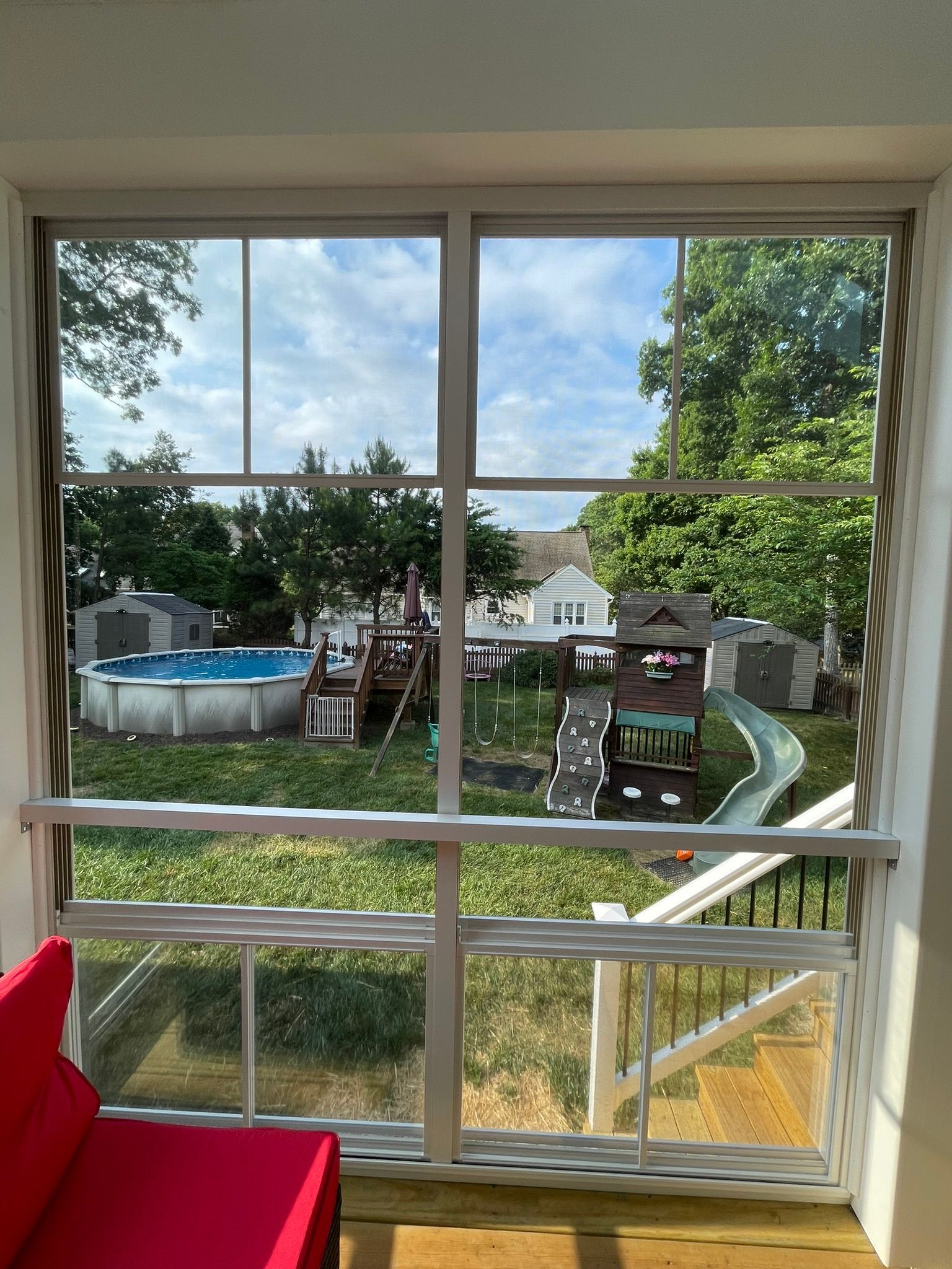View through a window to a backyard with a blue above-ground pool, trampoline, and green lawn