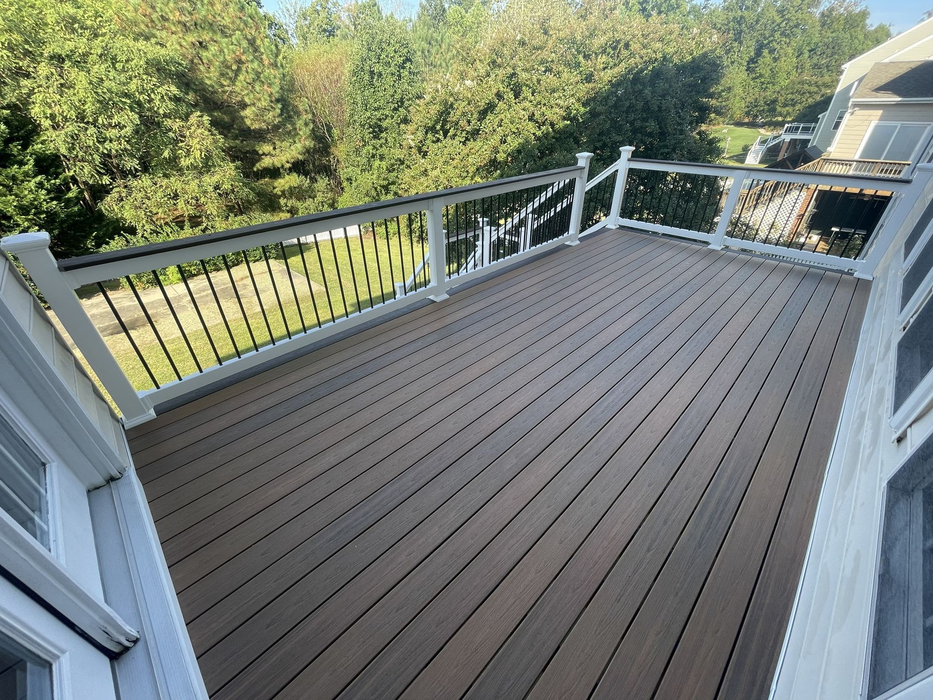 Wooden deck with white railings overlooking a green yard and trees